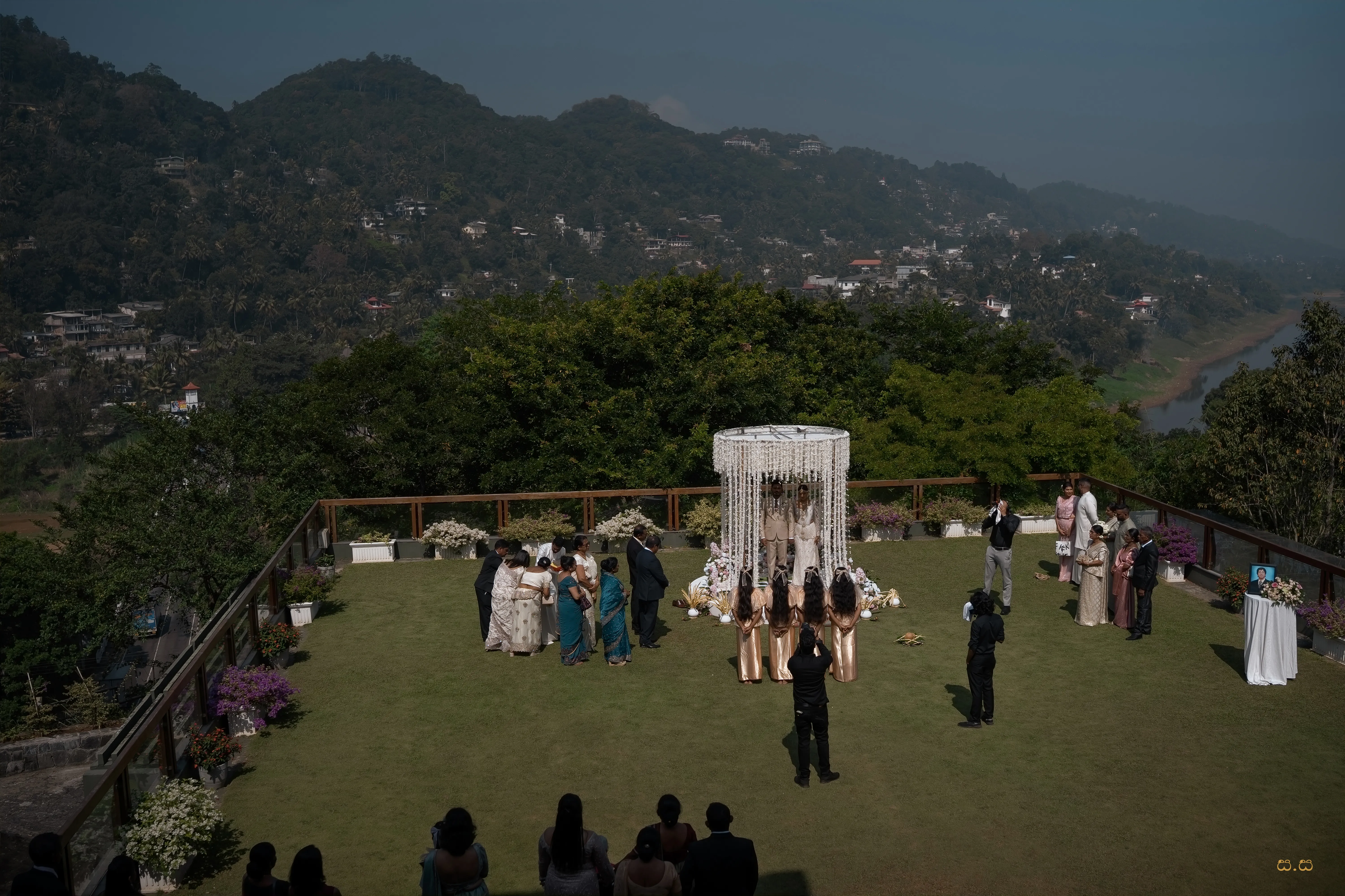 A wide view shows the open-air Poruwa ceremony against the mountain valley.