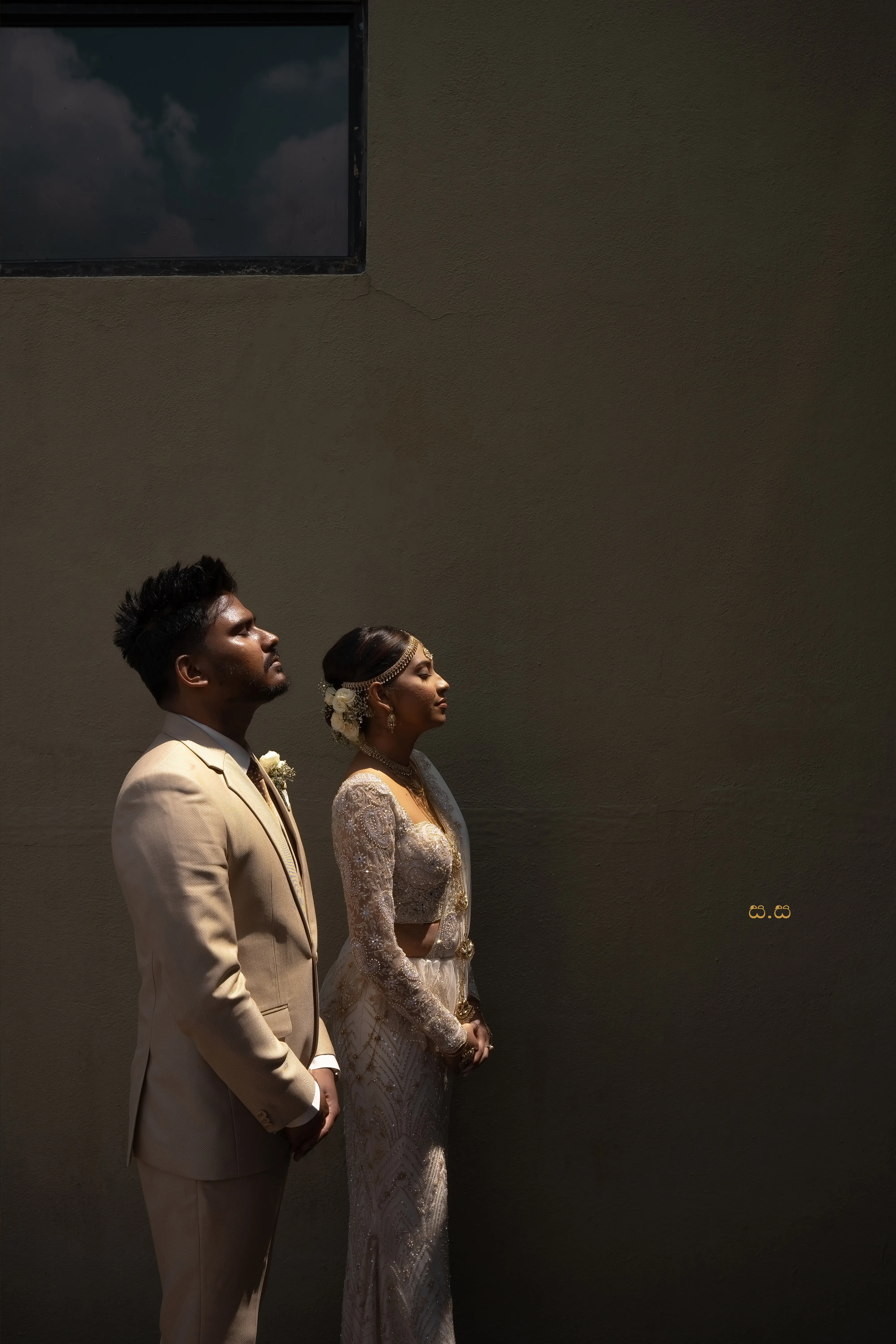 The couple share a quiet profile portrait against a deep shadowed wall.