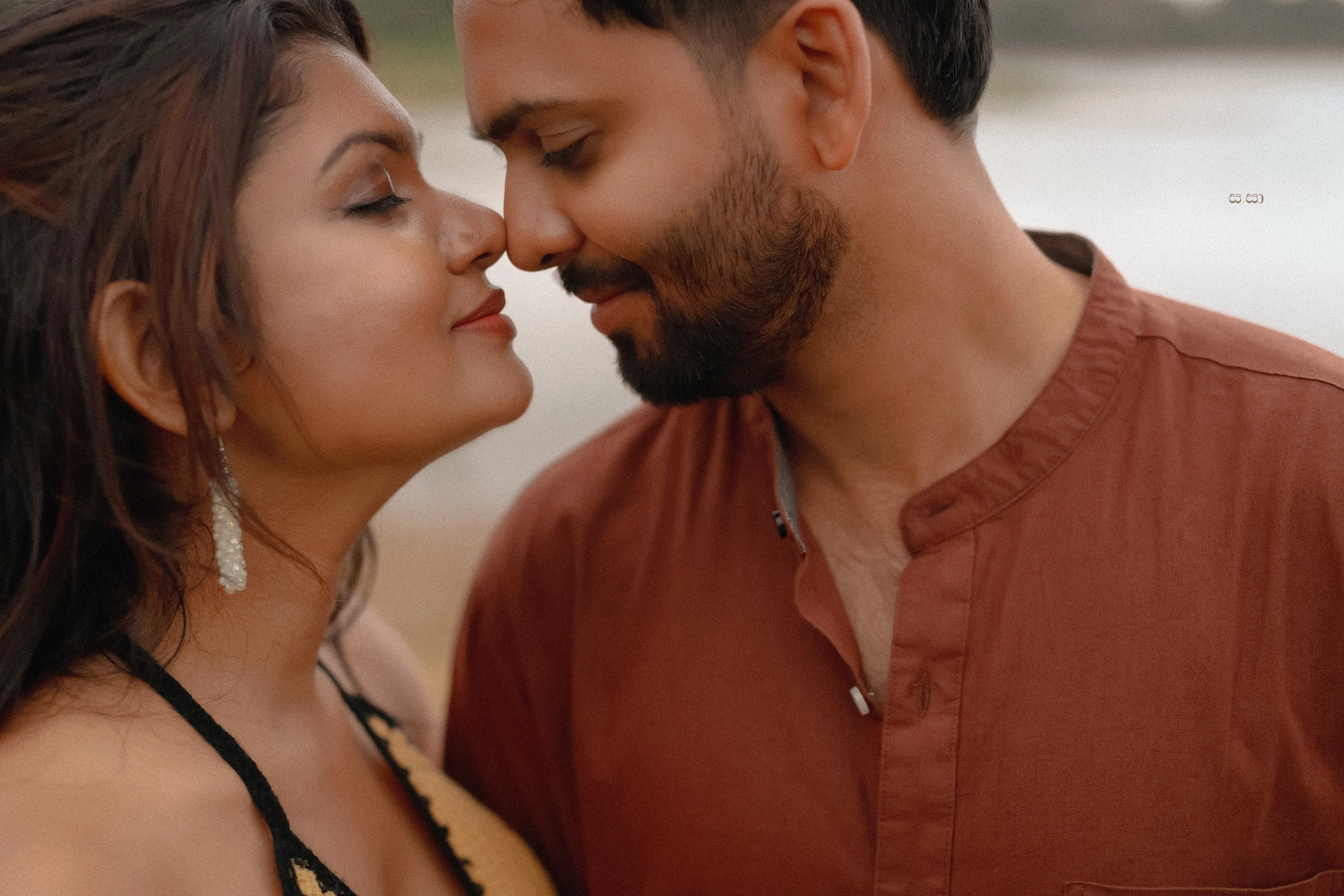 The couple leans close in warm rust and black styling by the water.