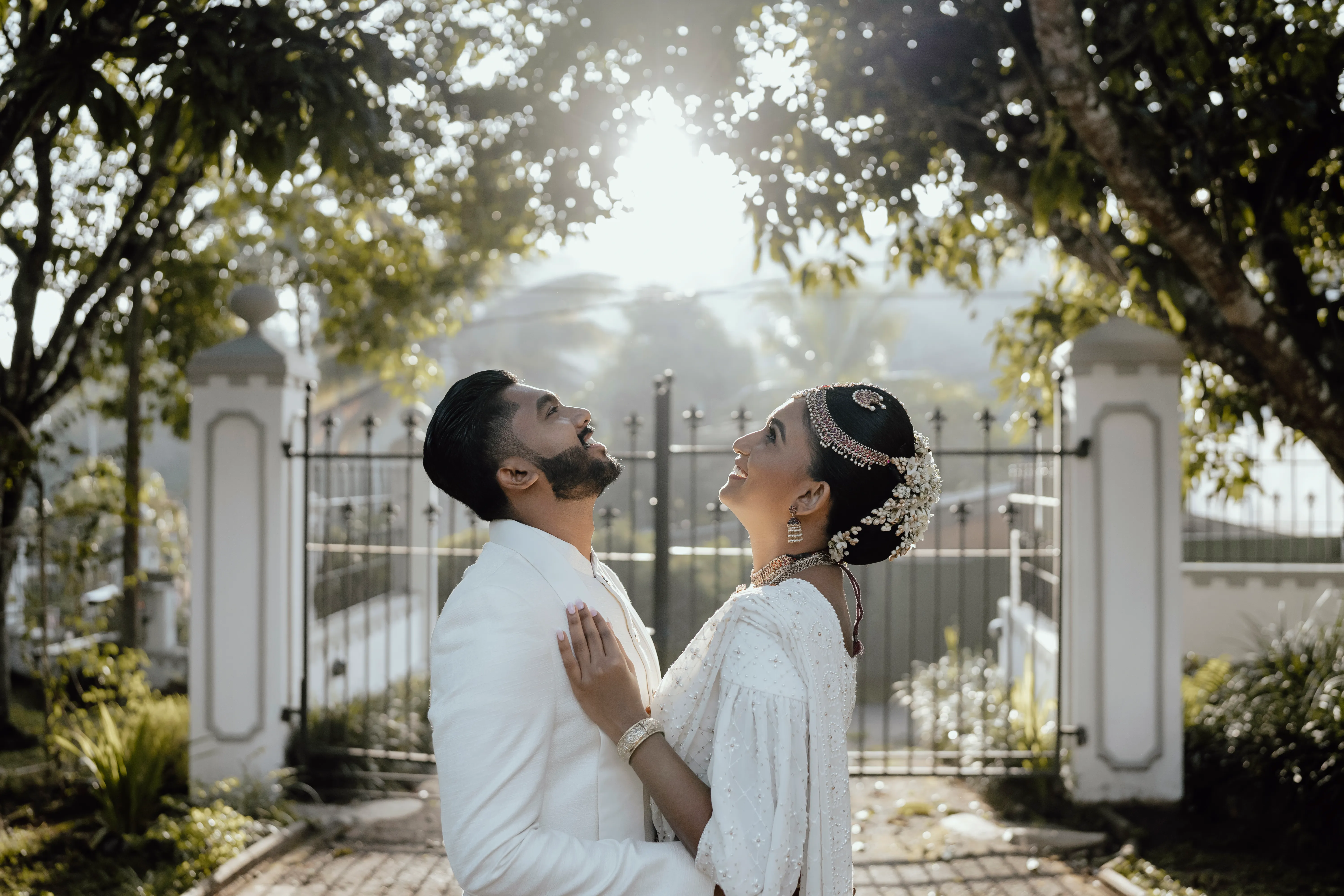 The couple looks upward together beneath the sculpted garden arch.