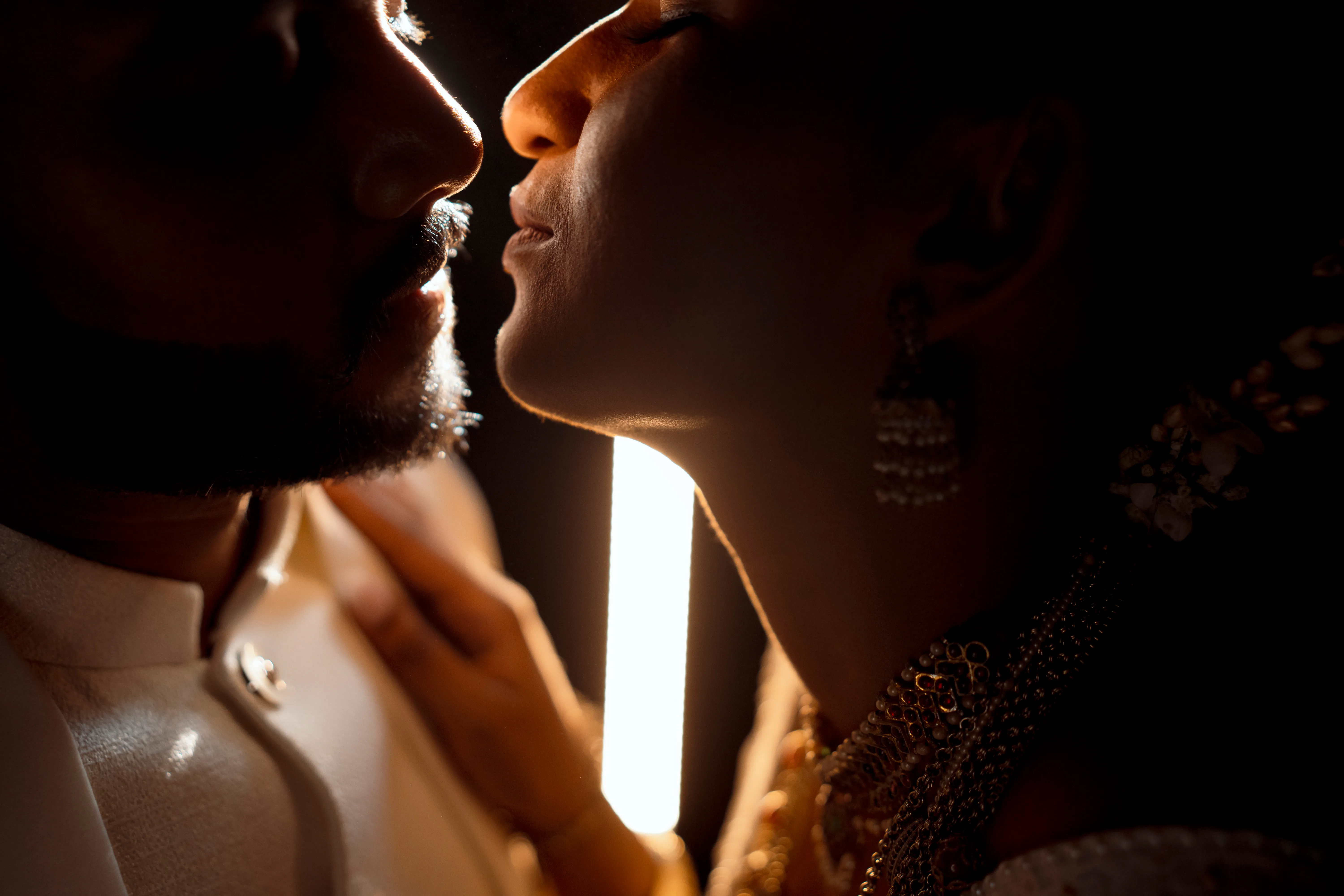The newlyweds lean toward one another beside a narrow beam of sunlight.