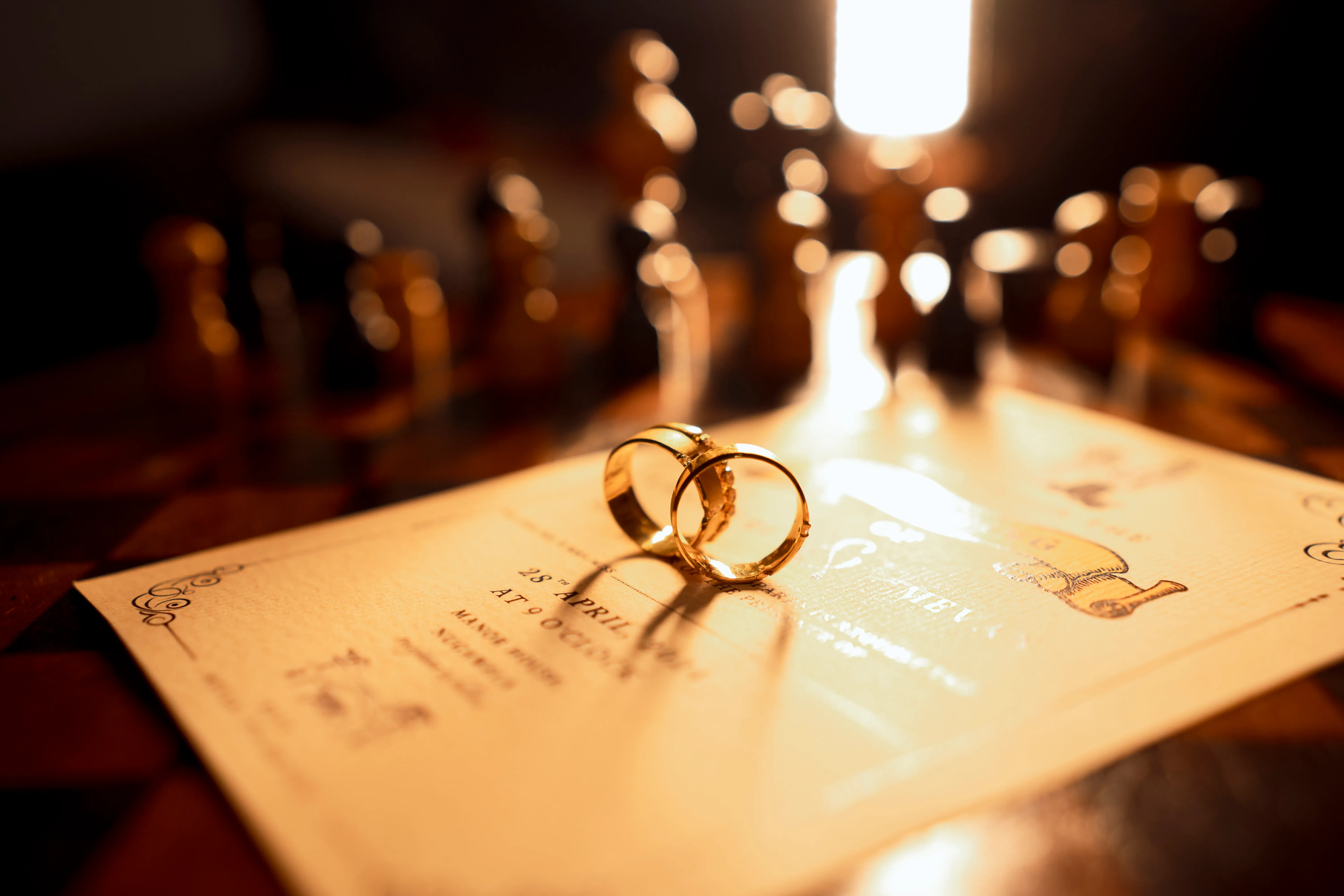 The wedding bands rest on the invitation as sunlight glows behind them.