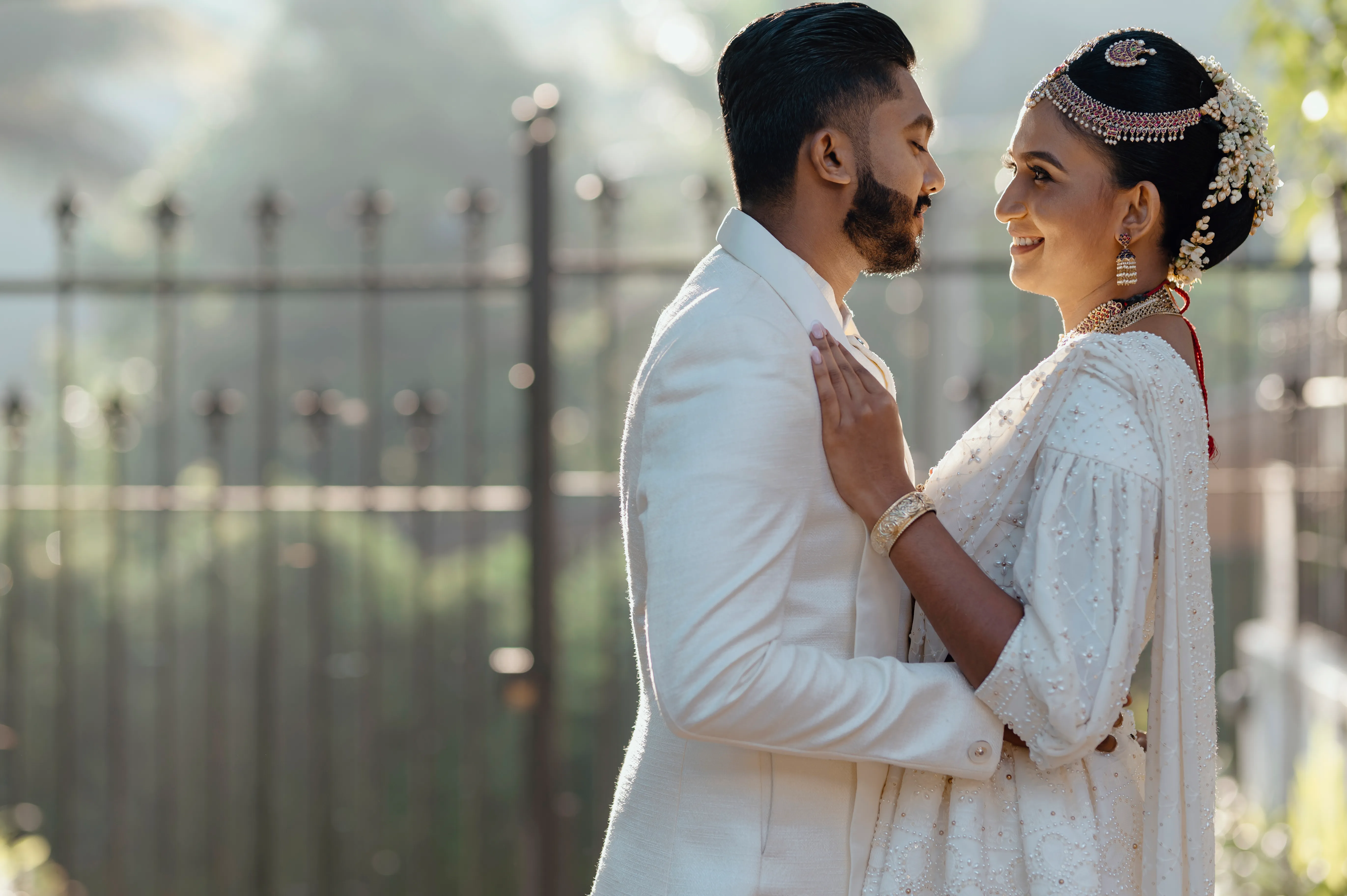 The couple face one another in soft sunlight beside the garden entrance.
