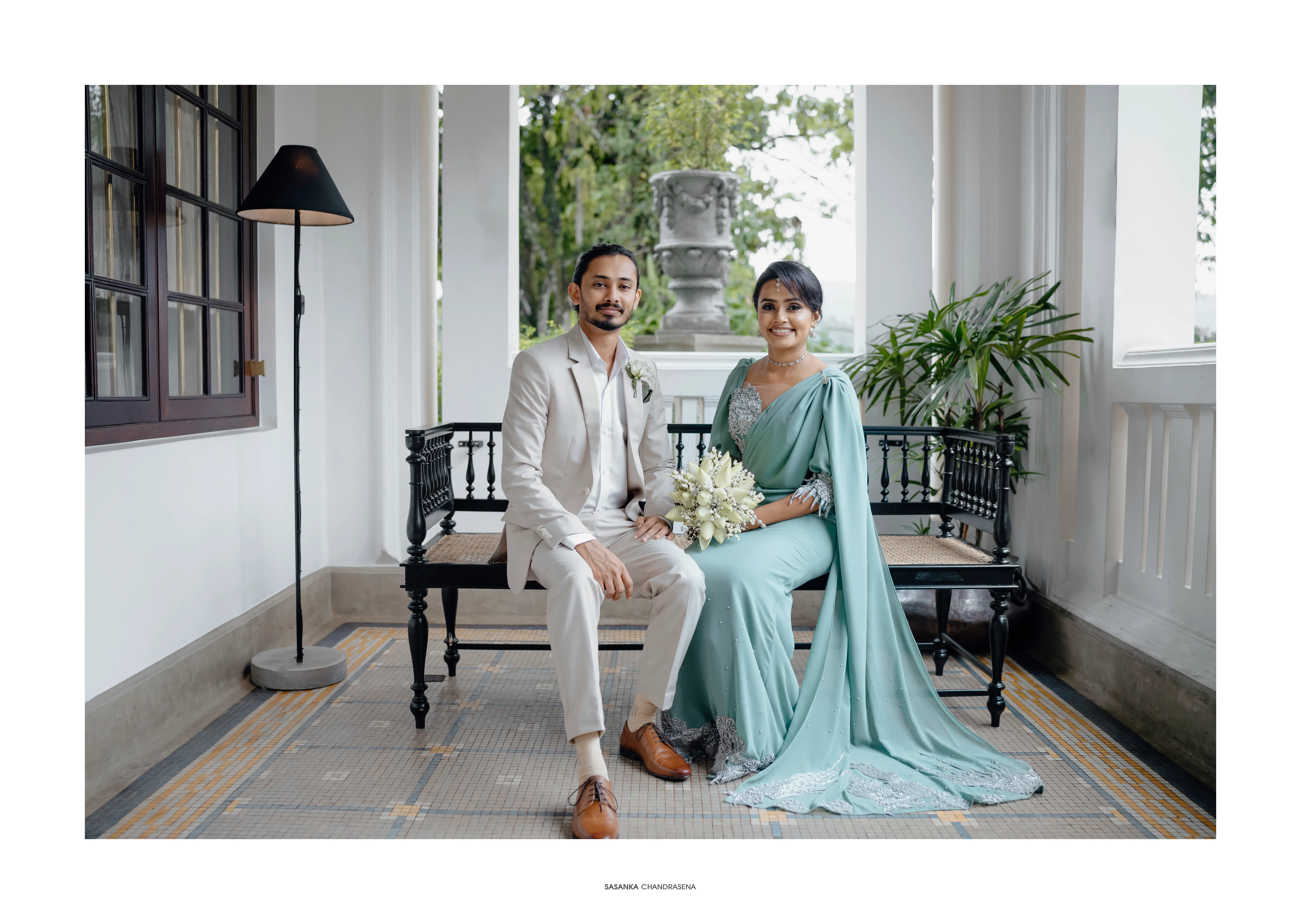 The engaged couple sits together on a shaded colonial-style veranda.