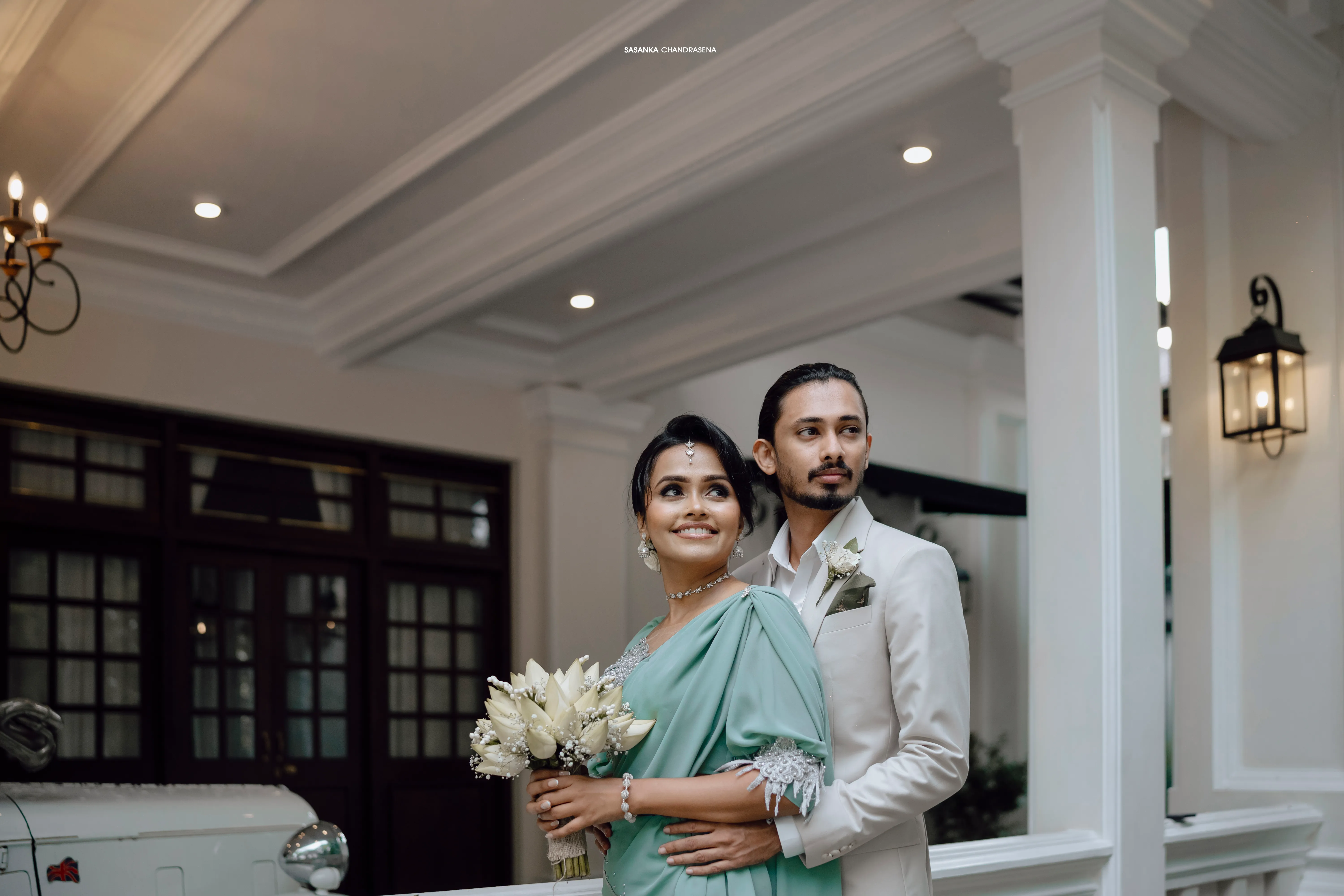 The engaged couple stands together with an ivory bouquet beneath the white portico.