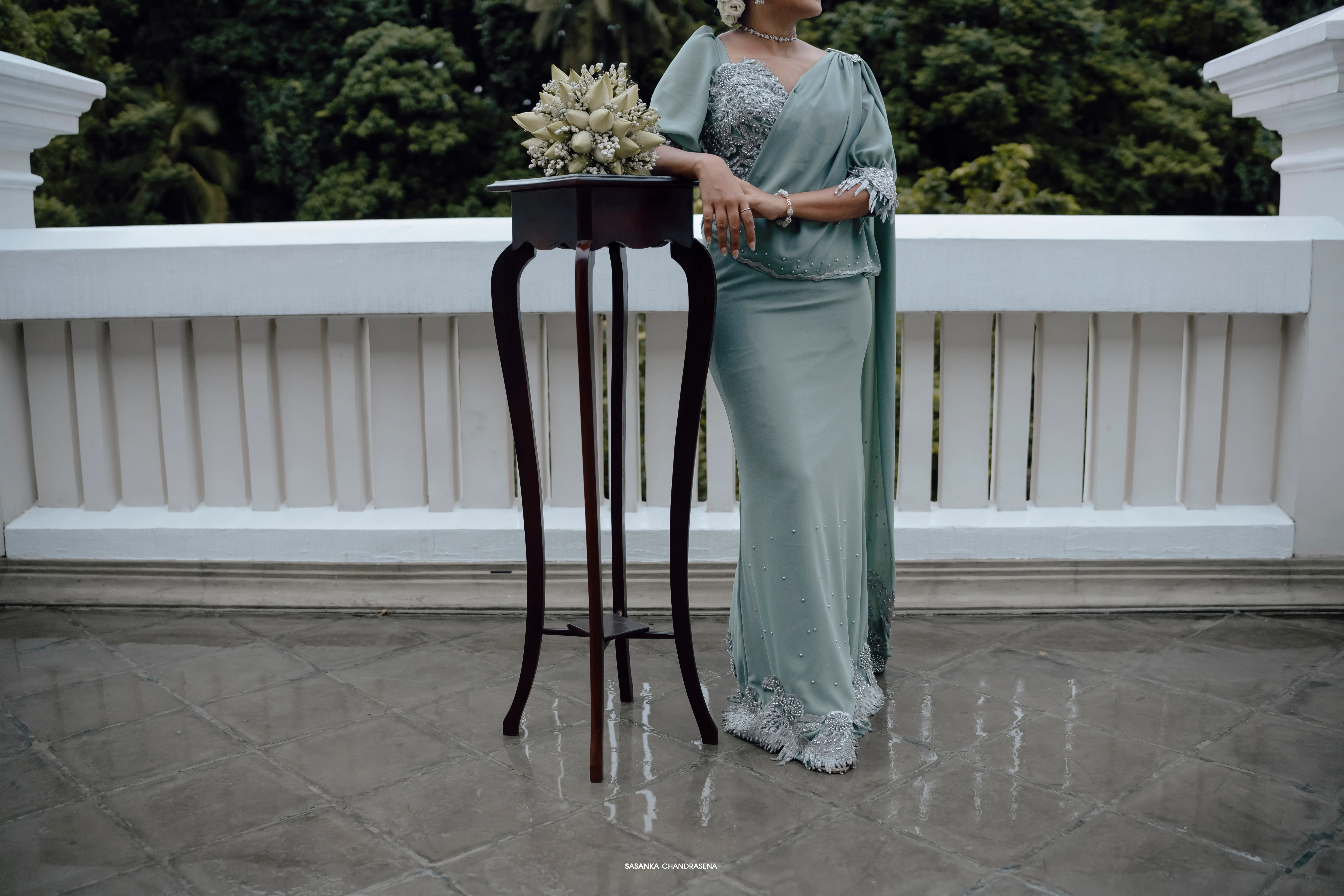 The bride-to-be stands at a dark wooden ceremony table decorated with pale flowers.