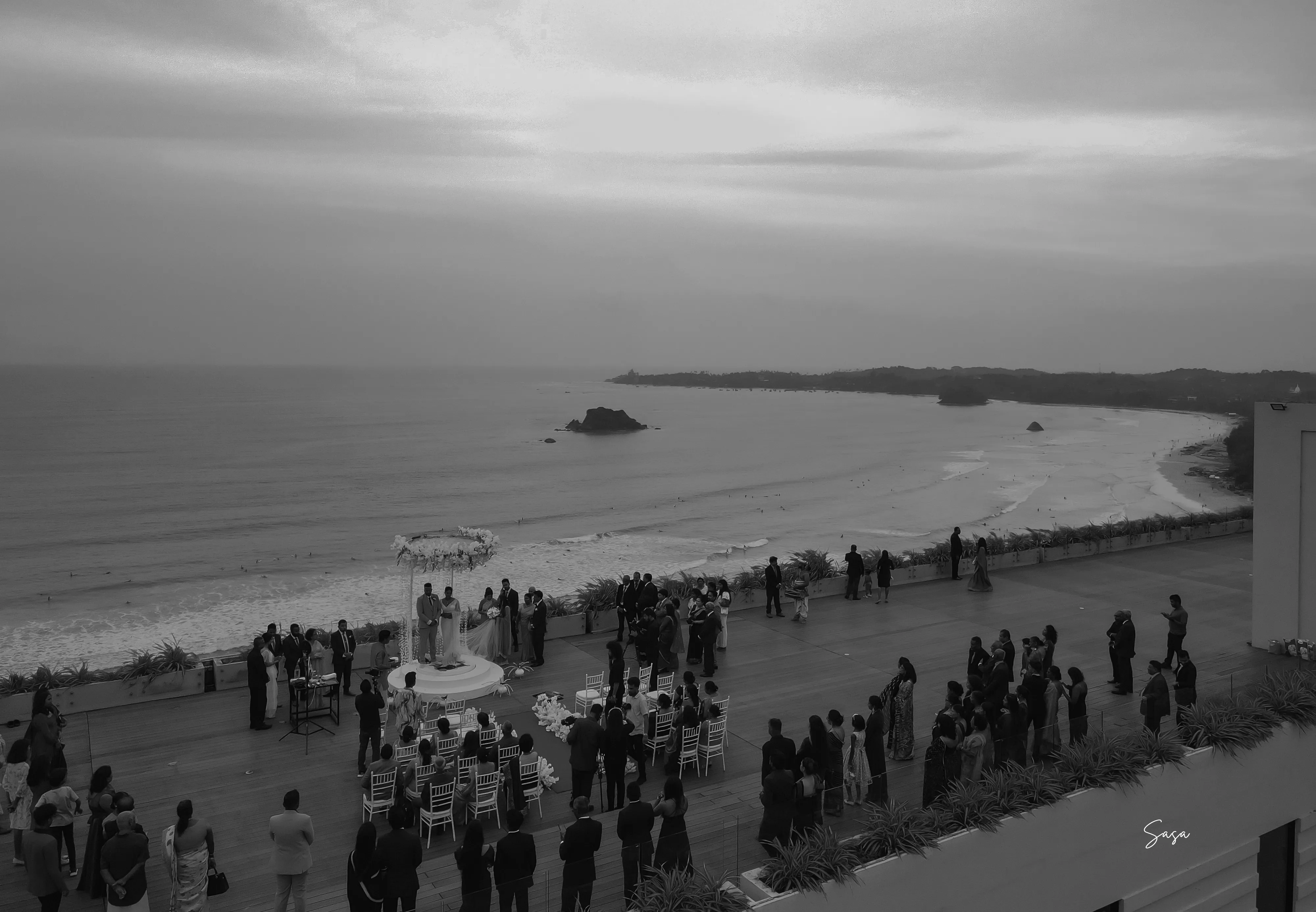 A wide monochrome view shows guests assembled along the coastal terrace.
