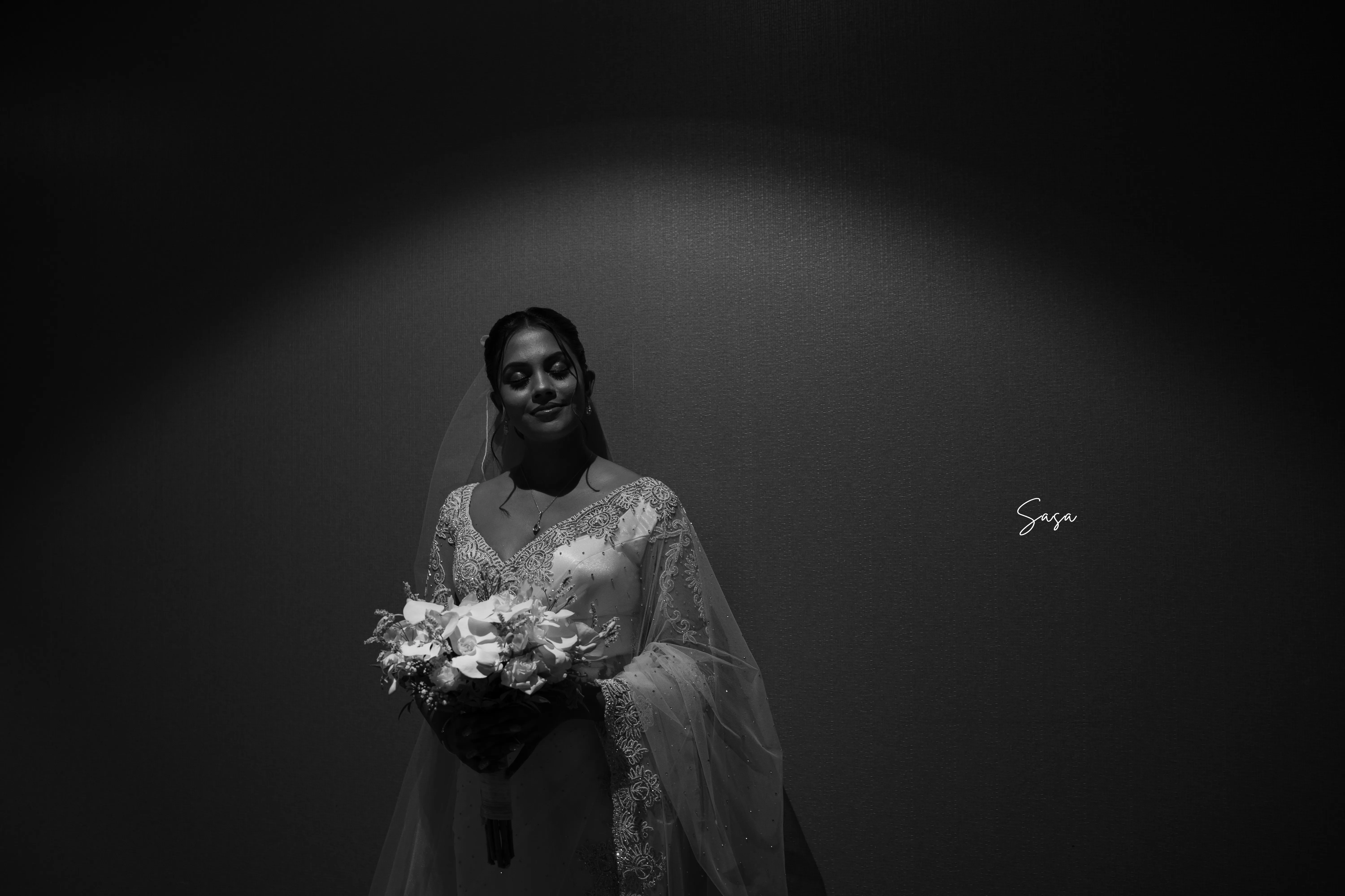 Harindi holds her bouquet in a dramatic monochrome studio portrait.
