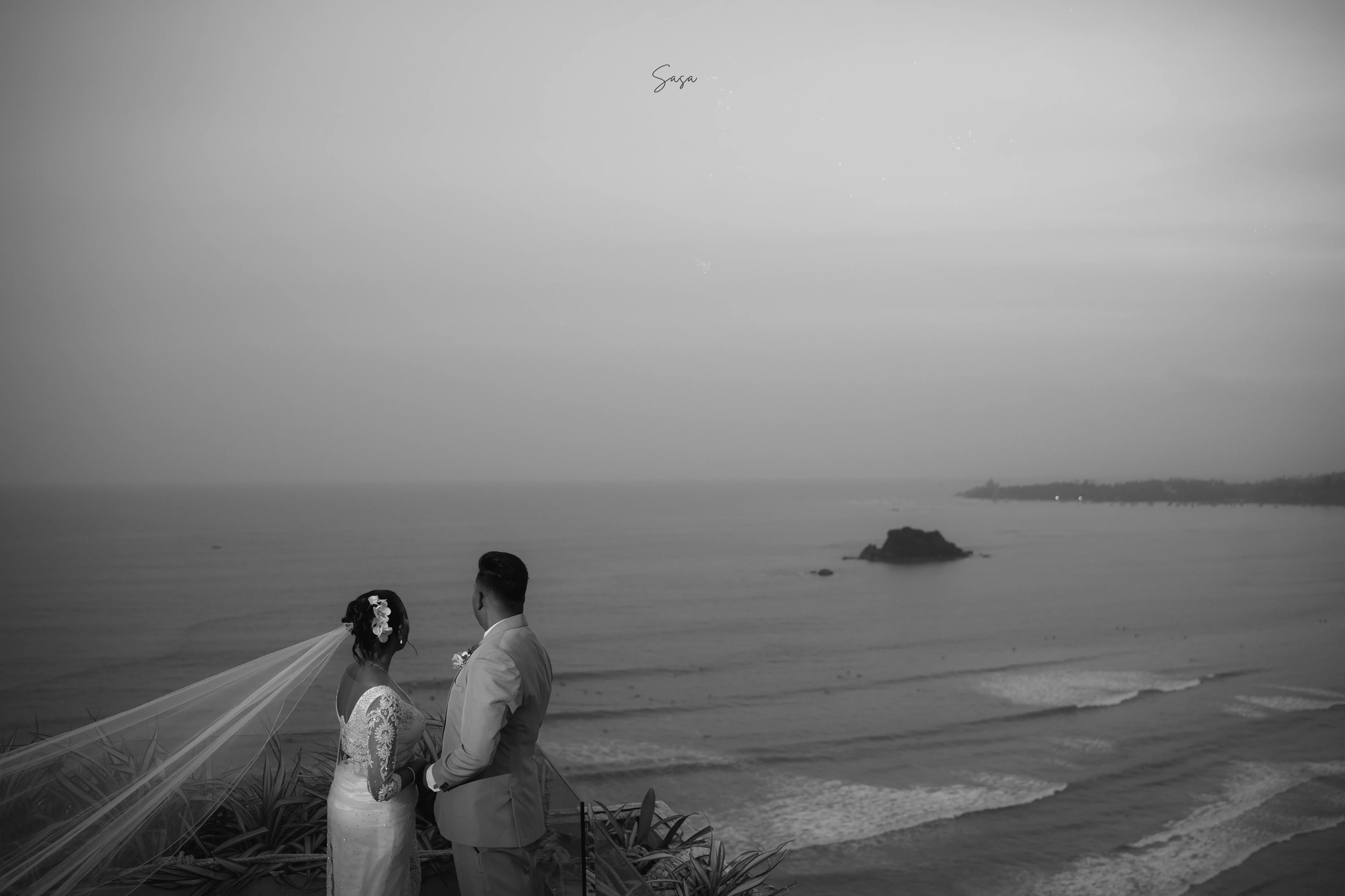 The newlyweds stand together above the sweeping shoreline in black and white.