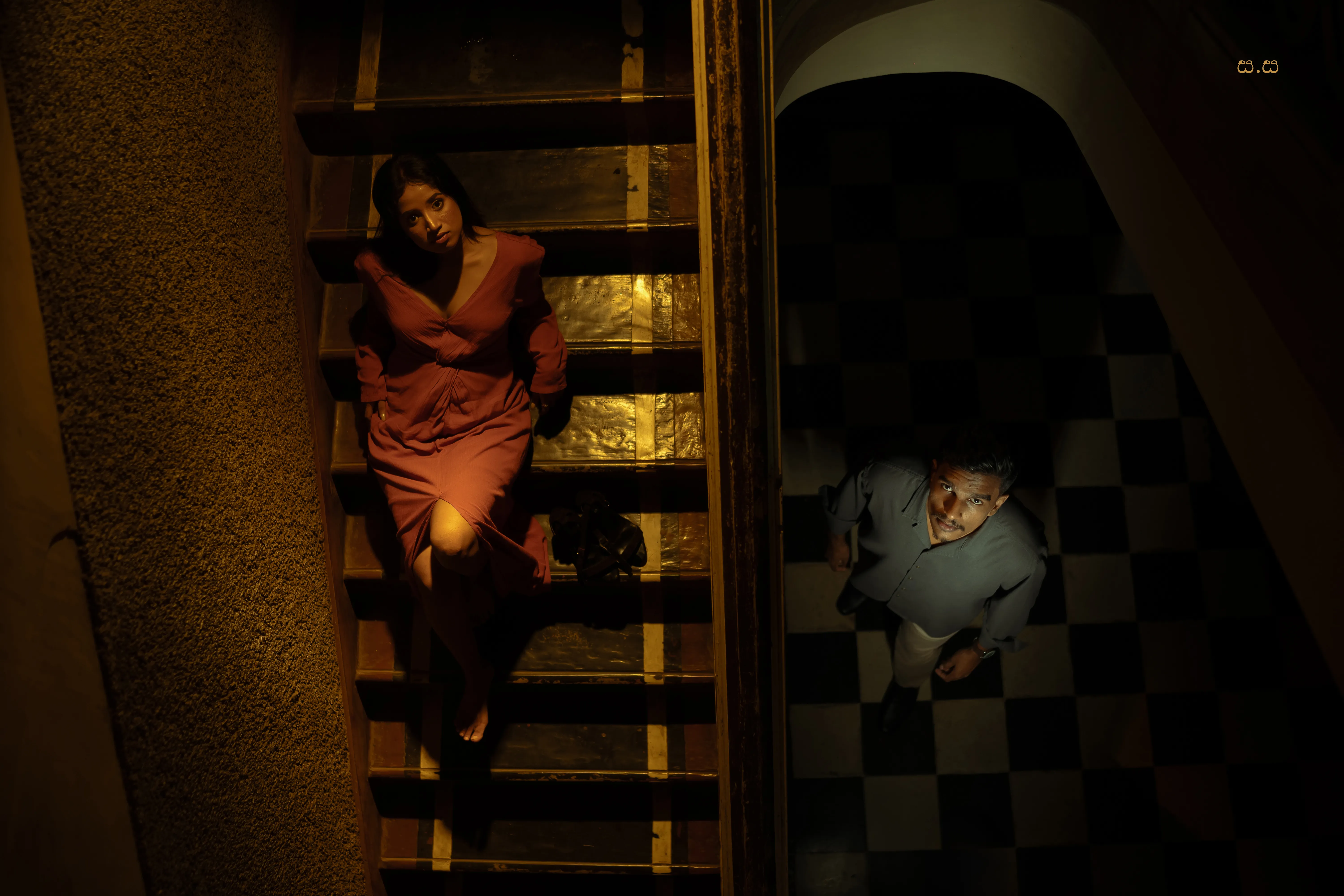 Hiruma and Naveen occupy different levels of a shadowed theatre stairwell.