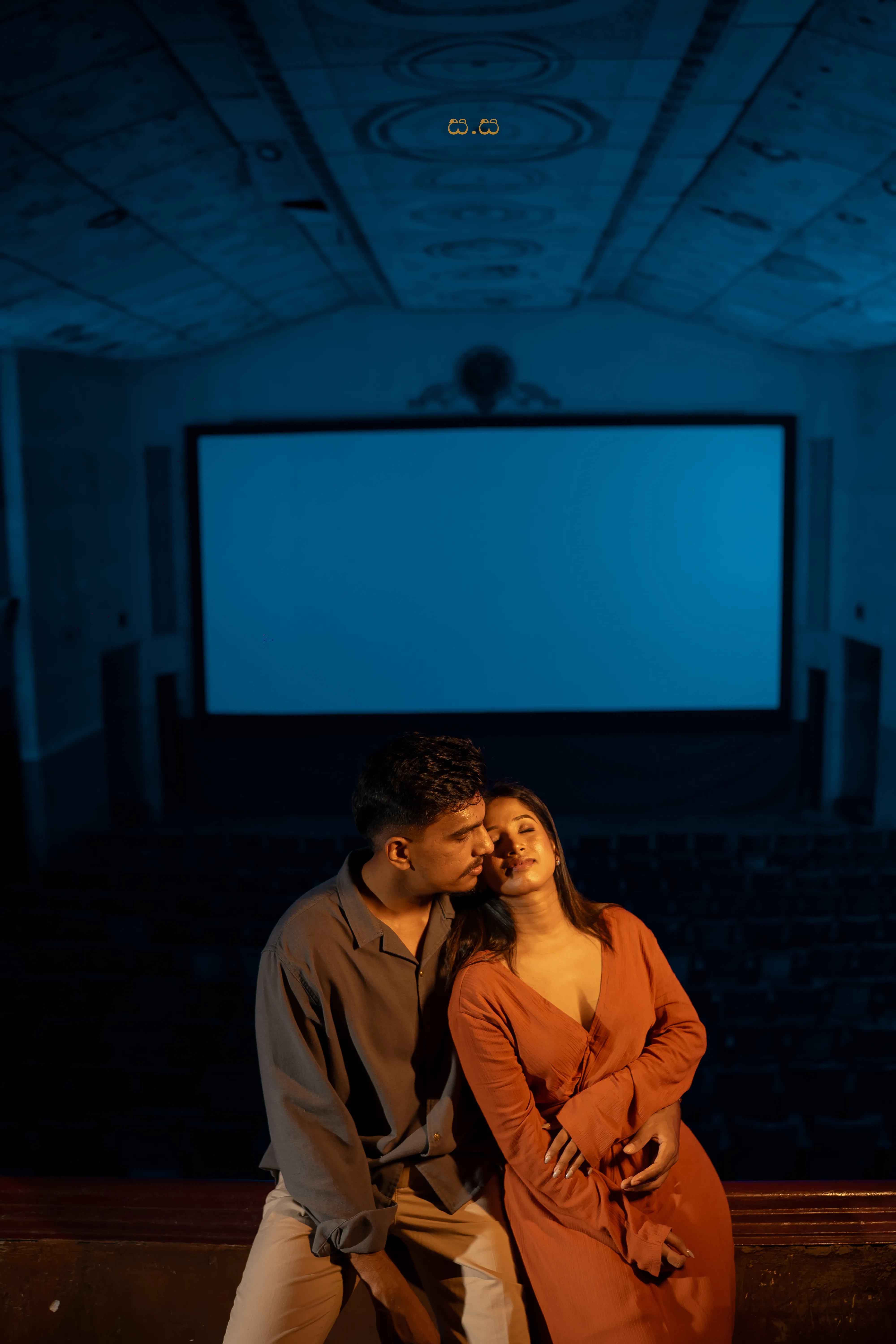 The couple sits shoulder to shoulder at the front of the auditorium.