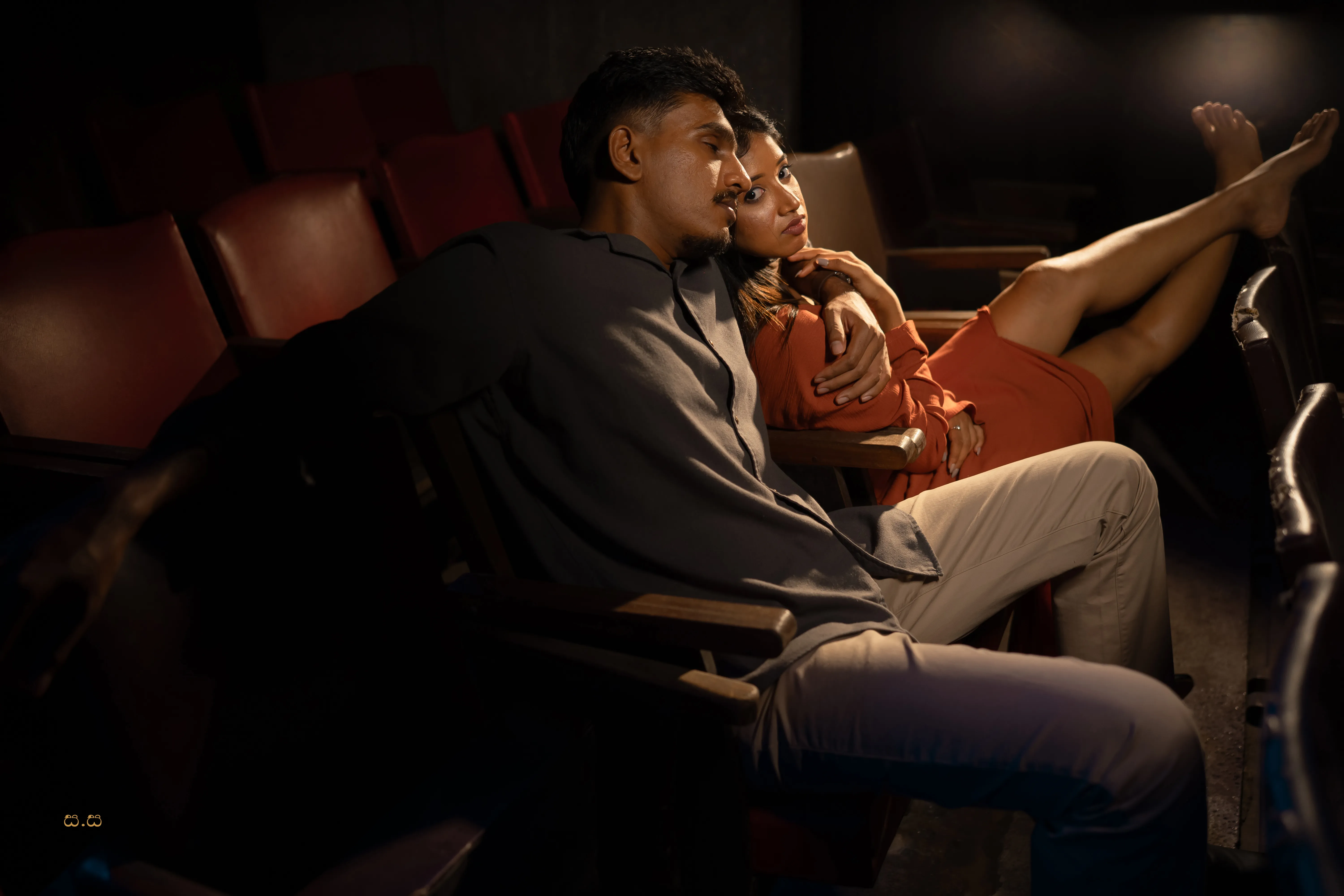 The couple reclines together across red seats in a cinematic pool of light.