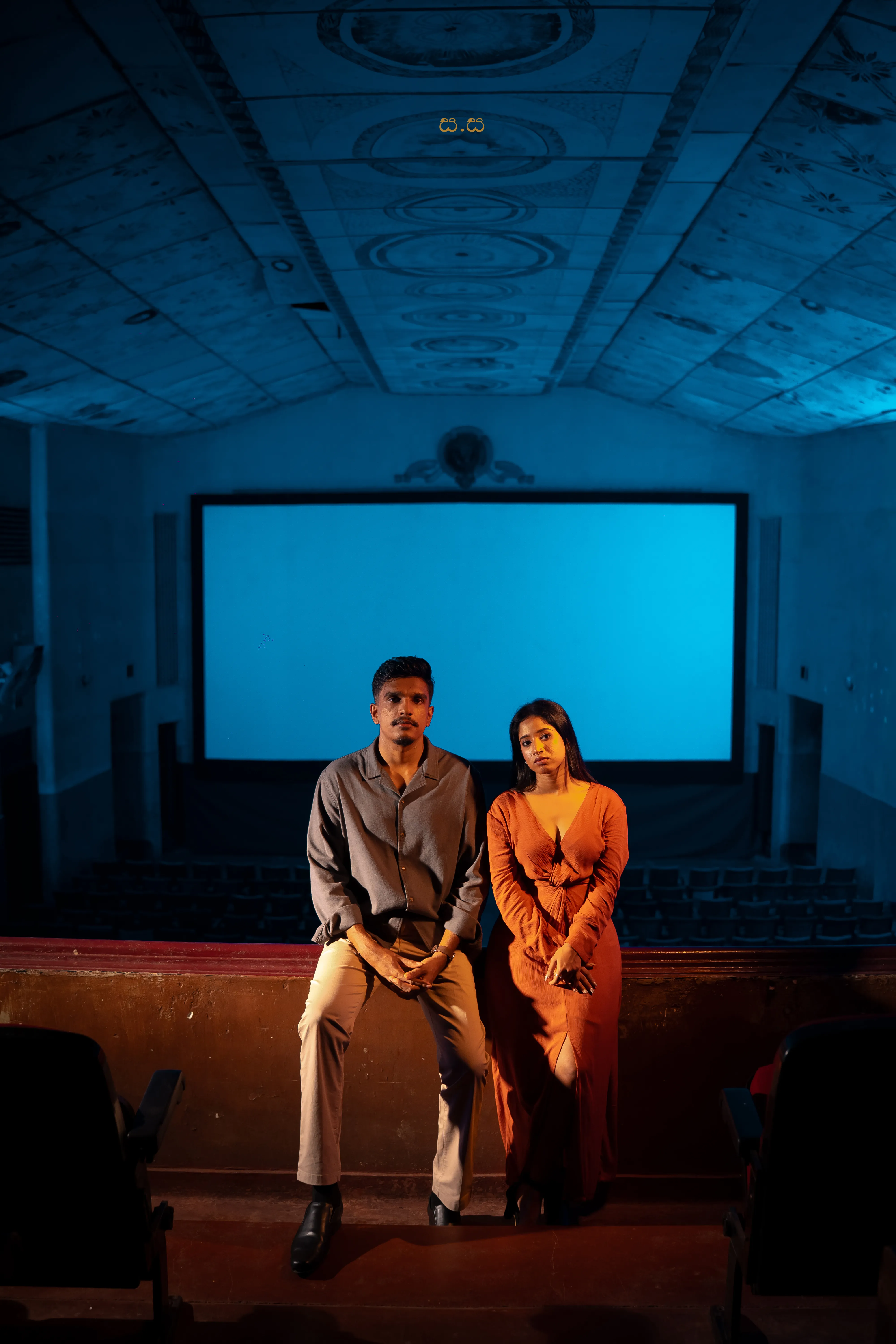 Hiruma and Naveen sit together beneath cool blue cinema light.