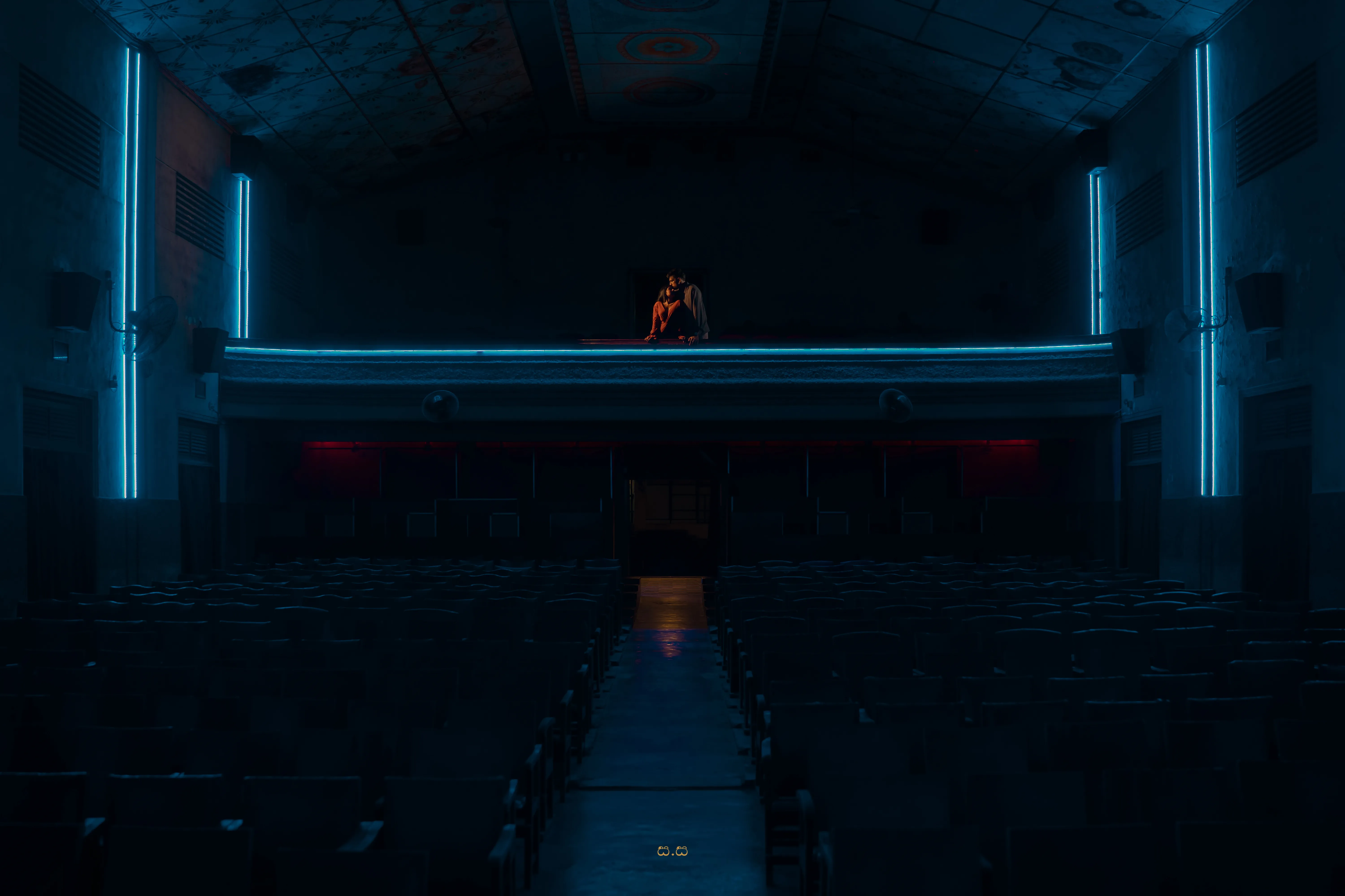 A wide blue-toned frame places the couple at the center of the vacant cinema.