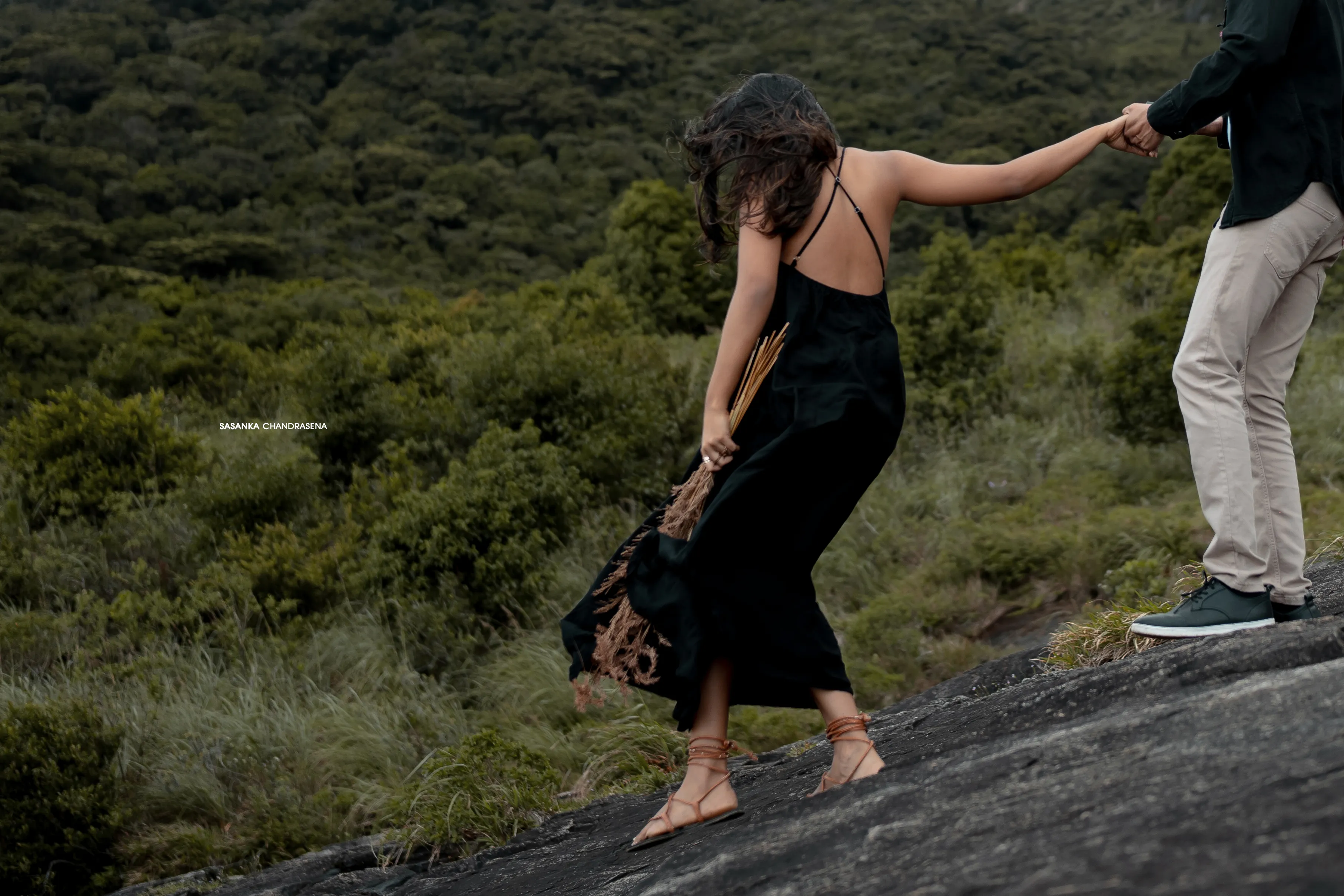 Iruka reaches back to guide Vidushi across a steep rocky slope.