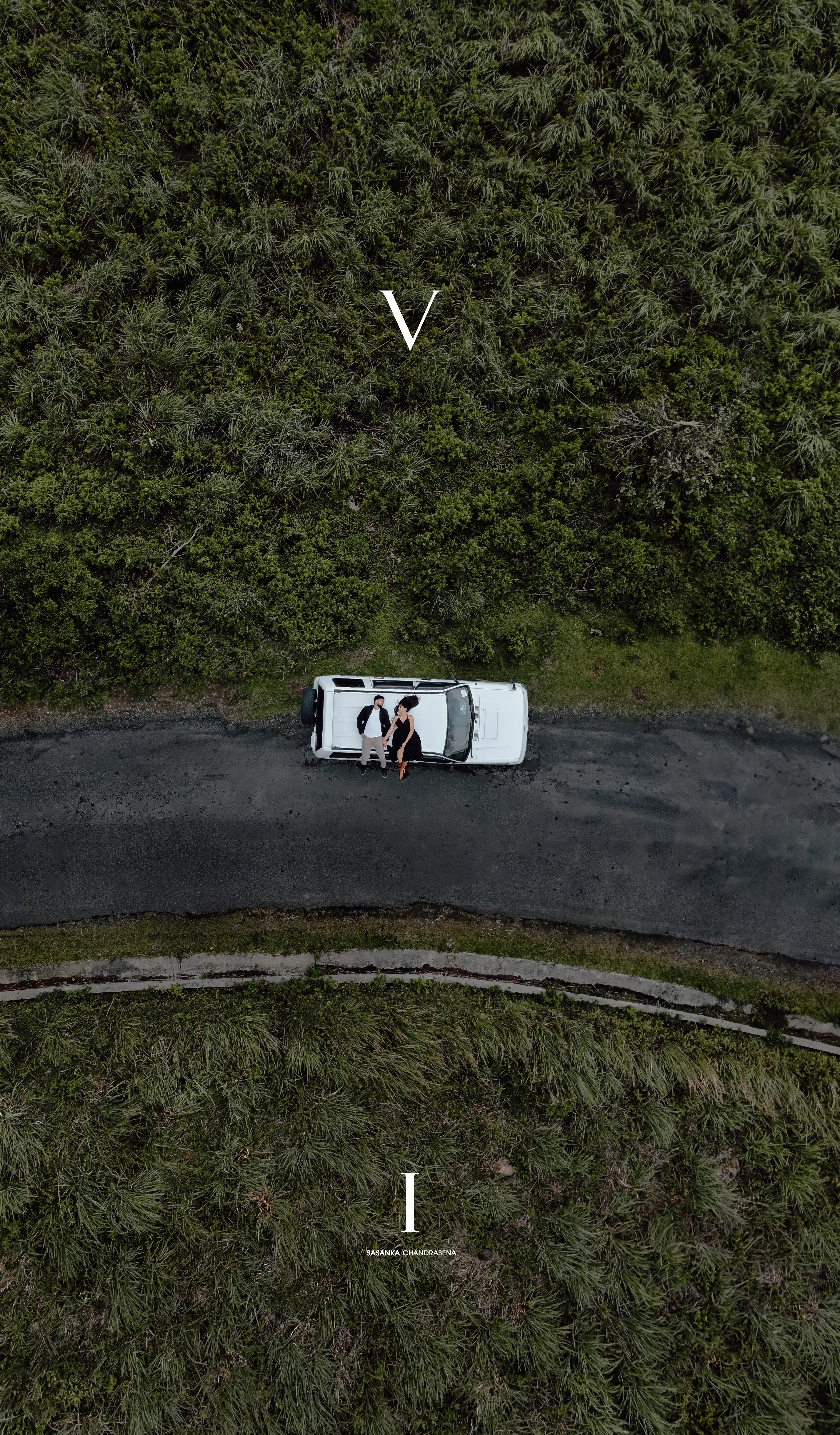 An aerial view places the couple and white SUV beside the mountain road.