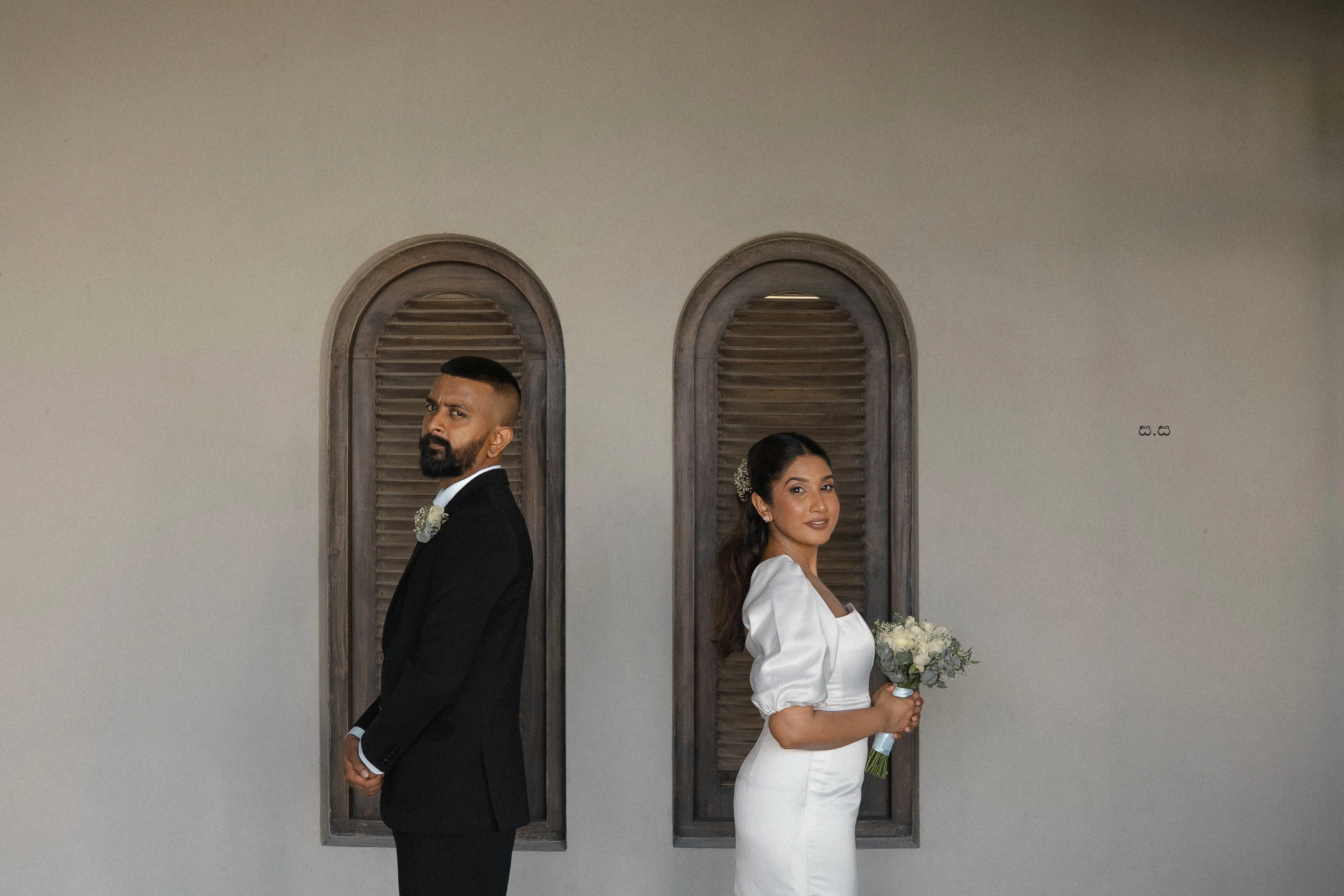 The couple stands in separate arched windows on a clean white facade.