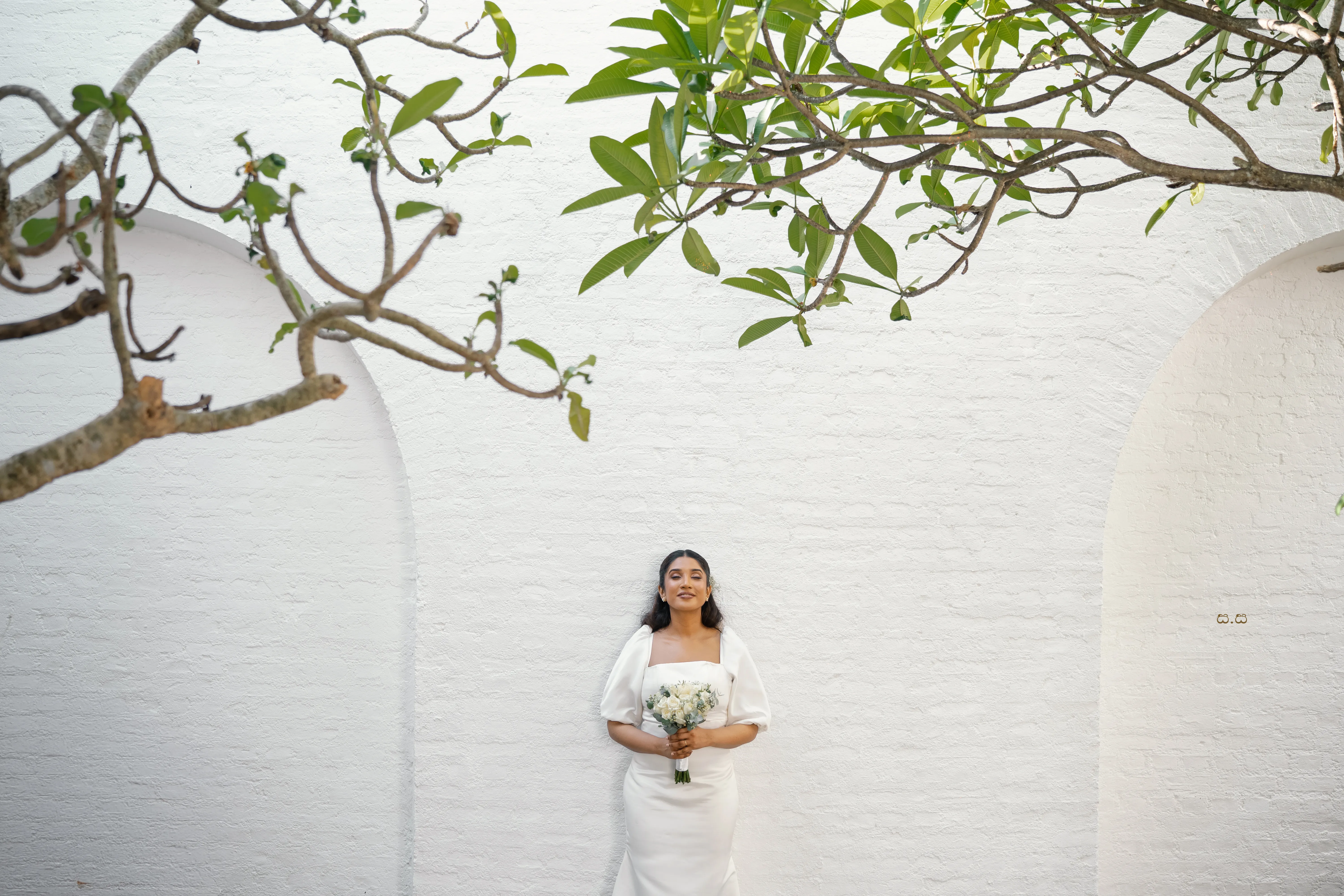 Malki is framed by a white wall, delicate branches, and open space.