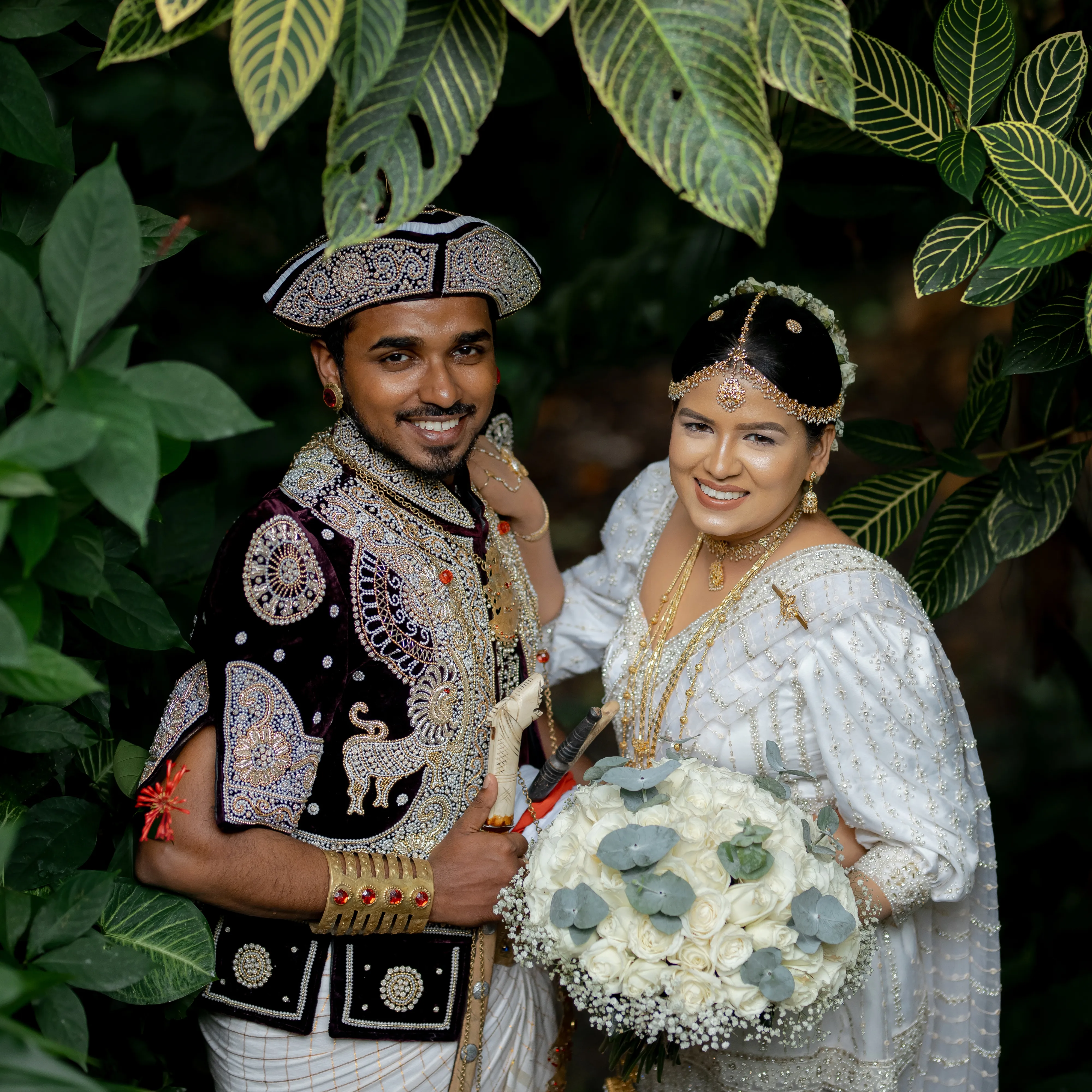 Nimasha and Bhashana smile together among deep tropical leaves.