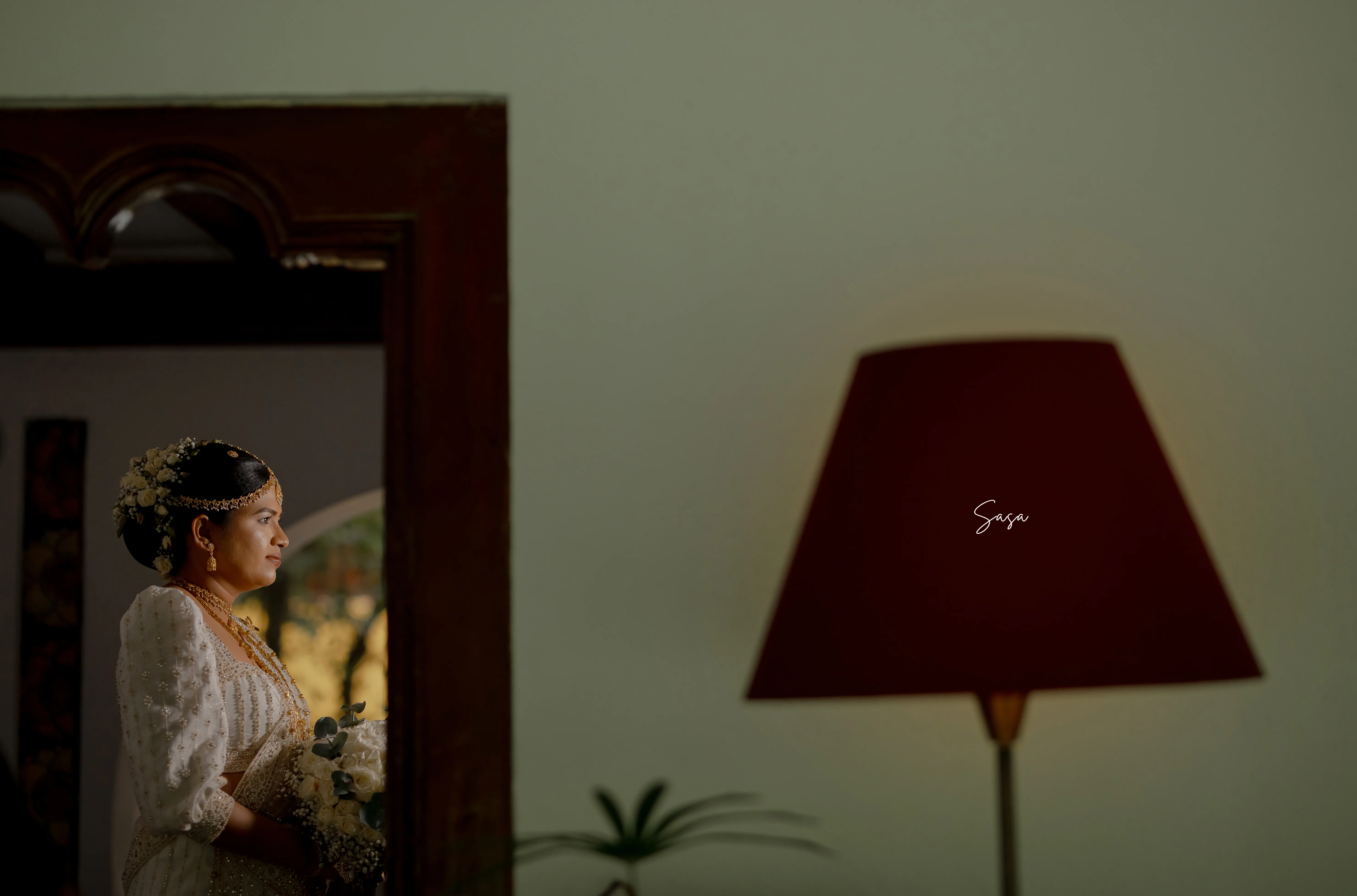 Nimasha is reflected beside a warm lamp inside the old residence.