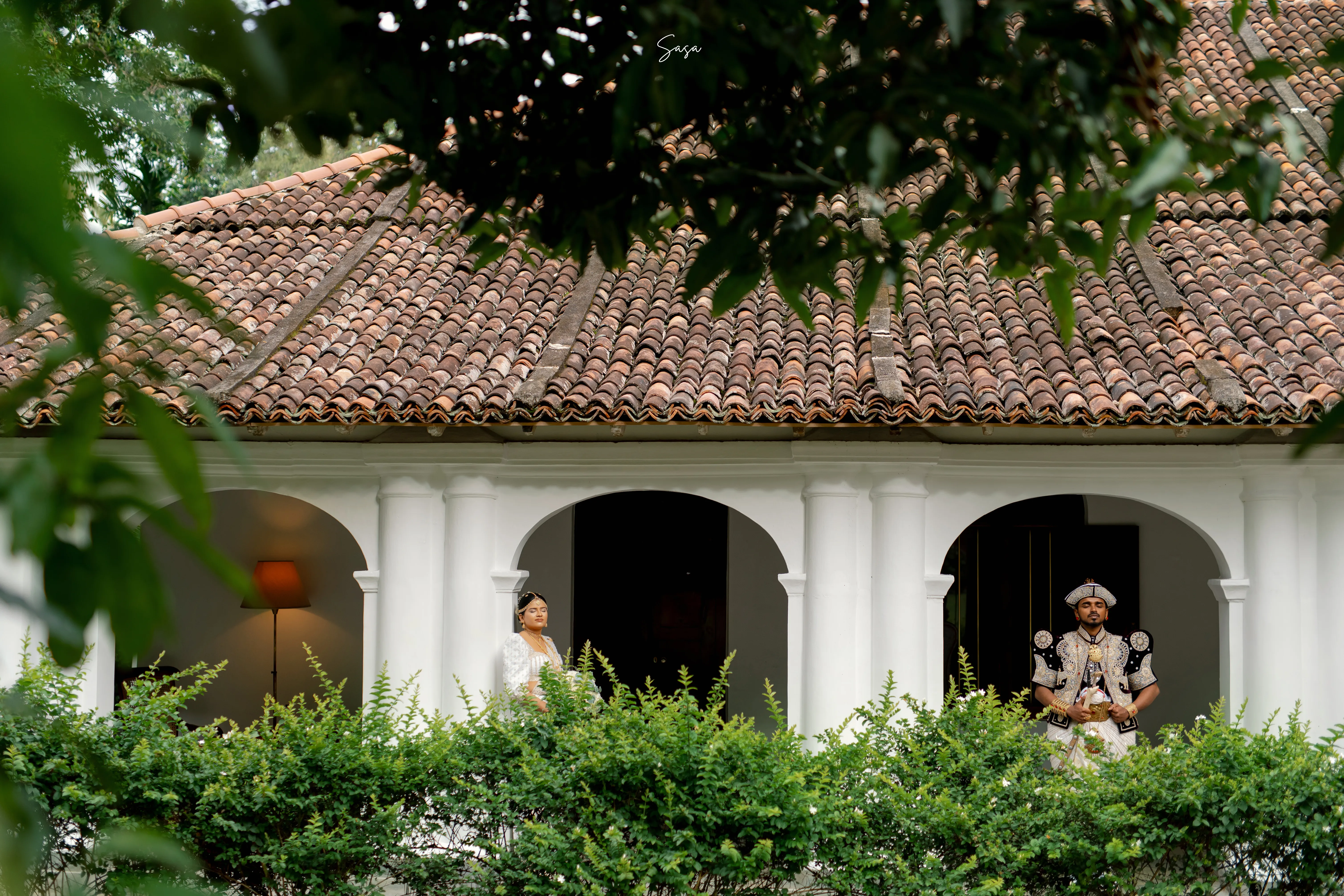 The couple appears beneath the arches of a whitewashed colonial residence.