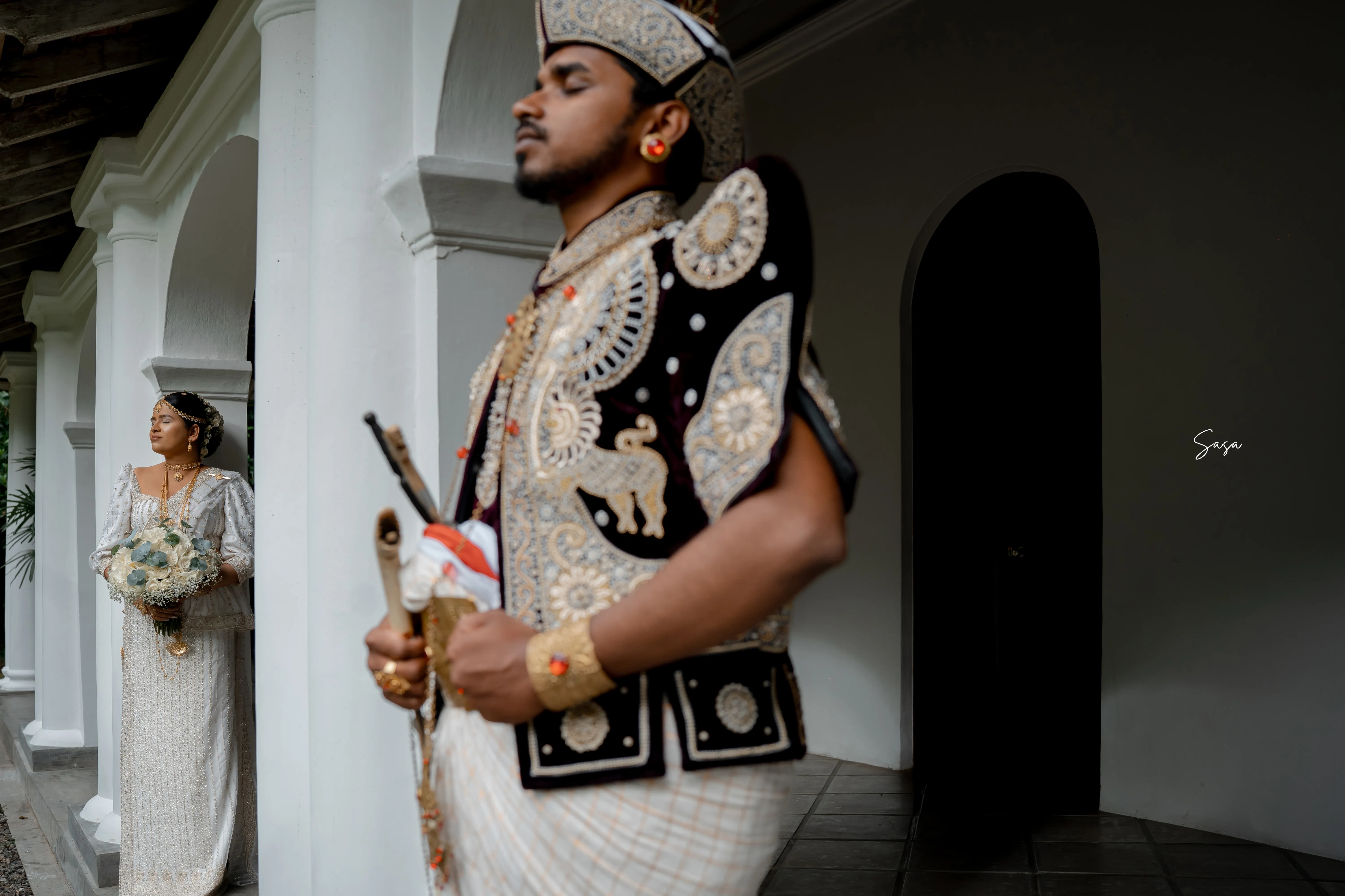 Bhashana stands in ceremonial dress between the manor’s white columns.