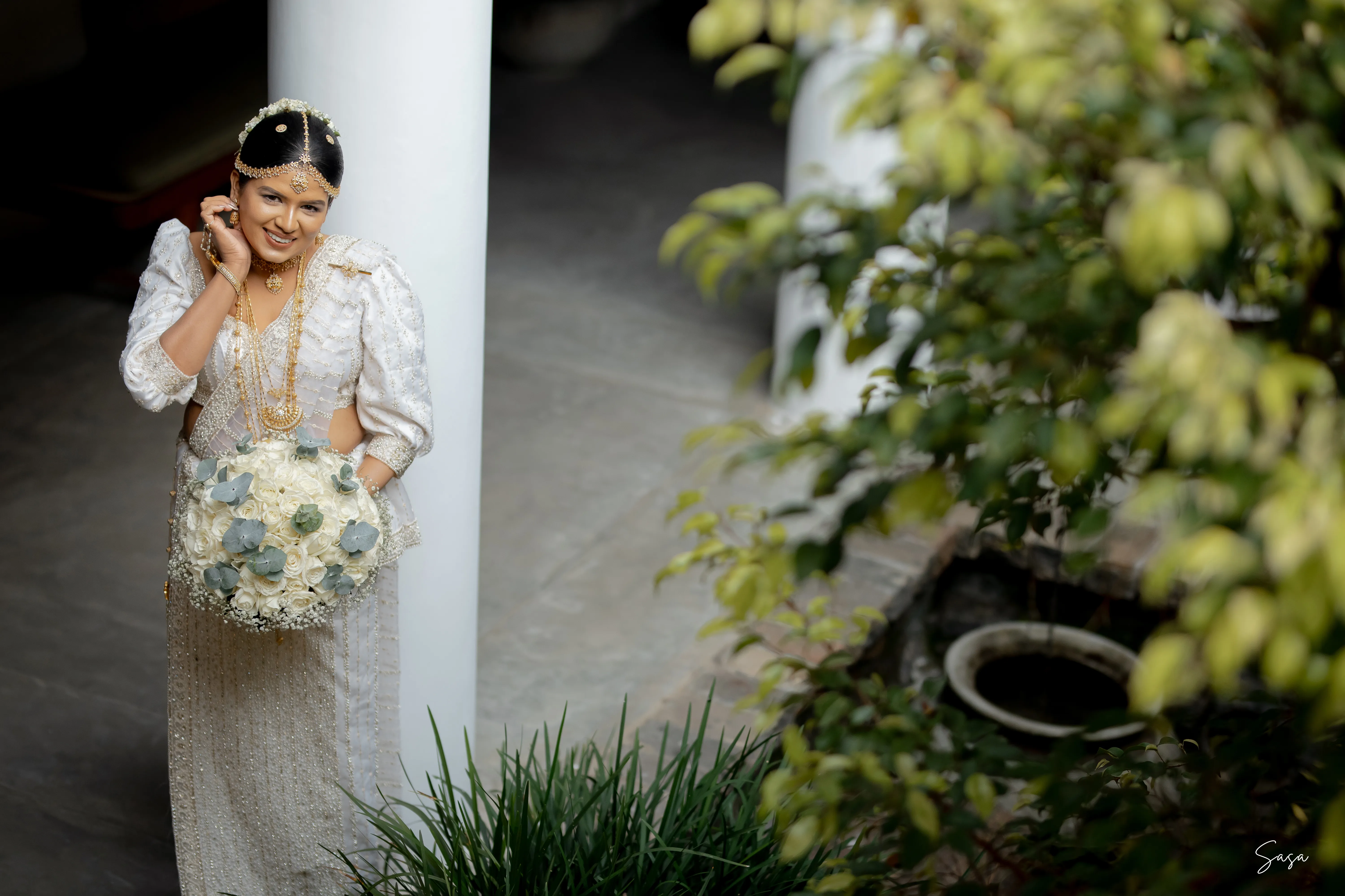 Nimasha walks through the shaded garden carrying a pale blue and white bouquet.