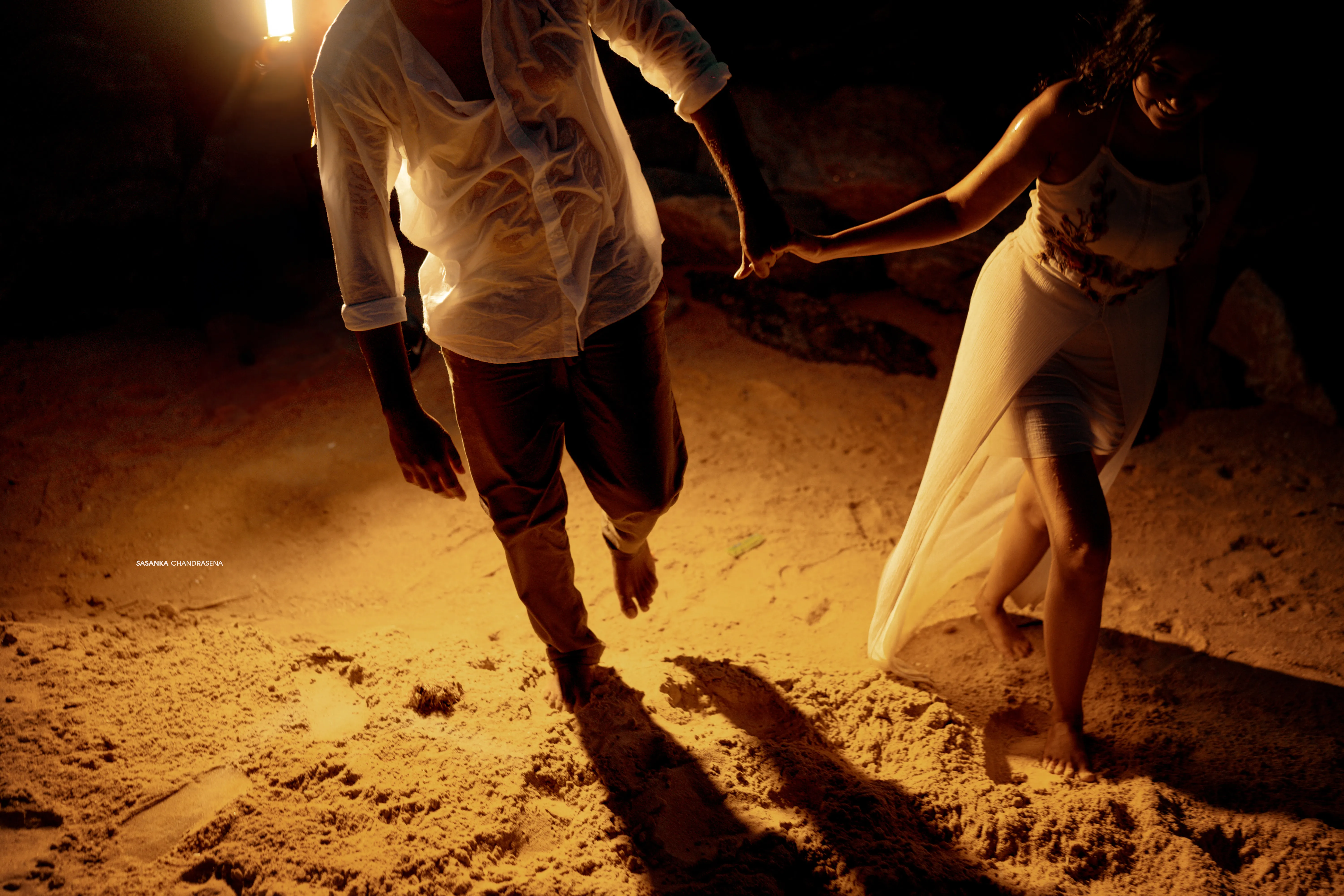 Sanka and Warunima dance barefoot on the beach beneath warm amber light.