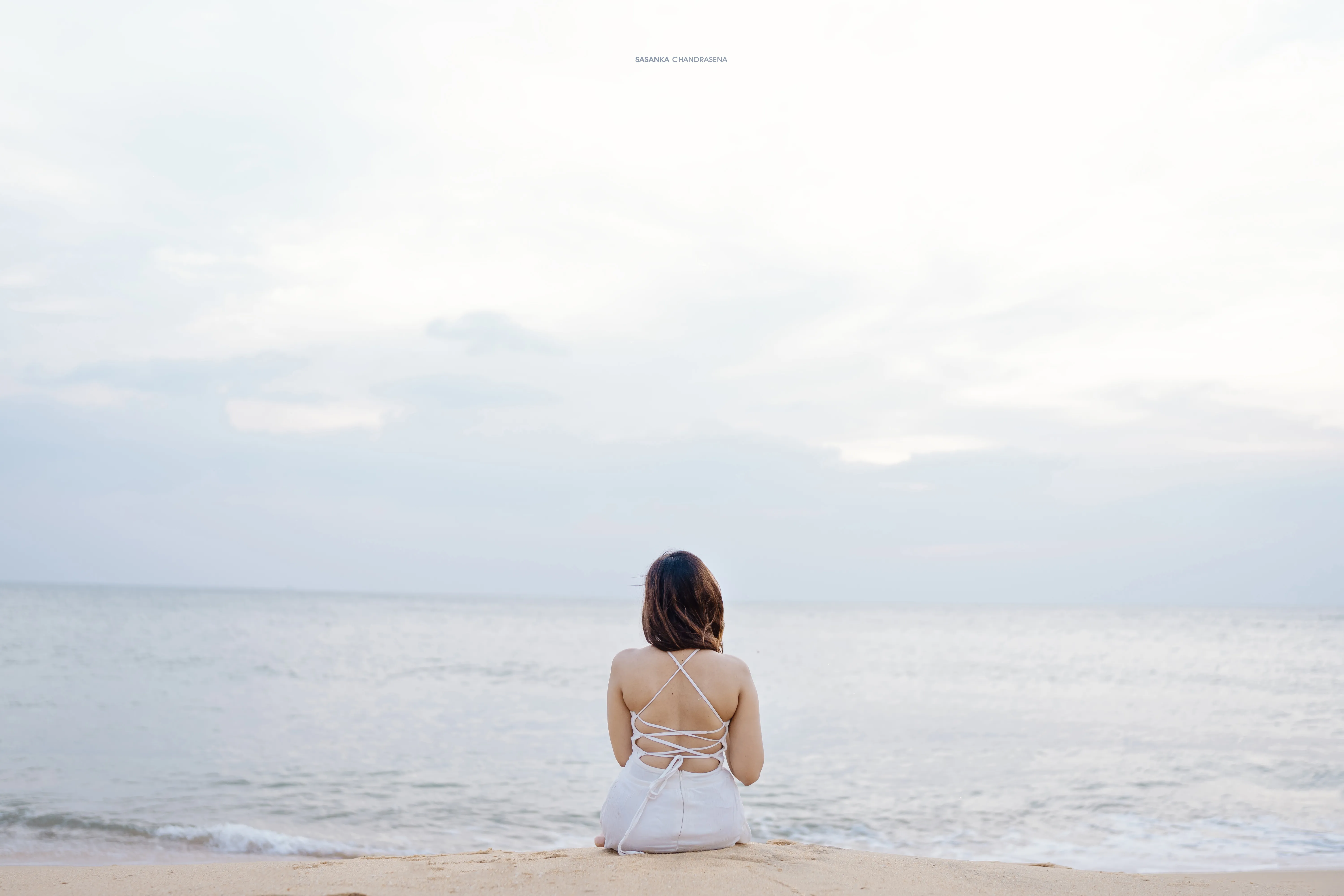 Warunima sits facing the quiet ocean beneath a pale sky.
