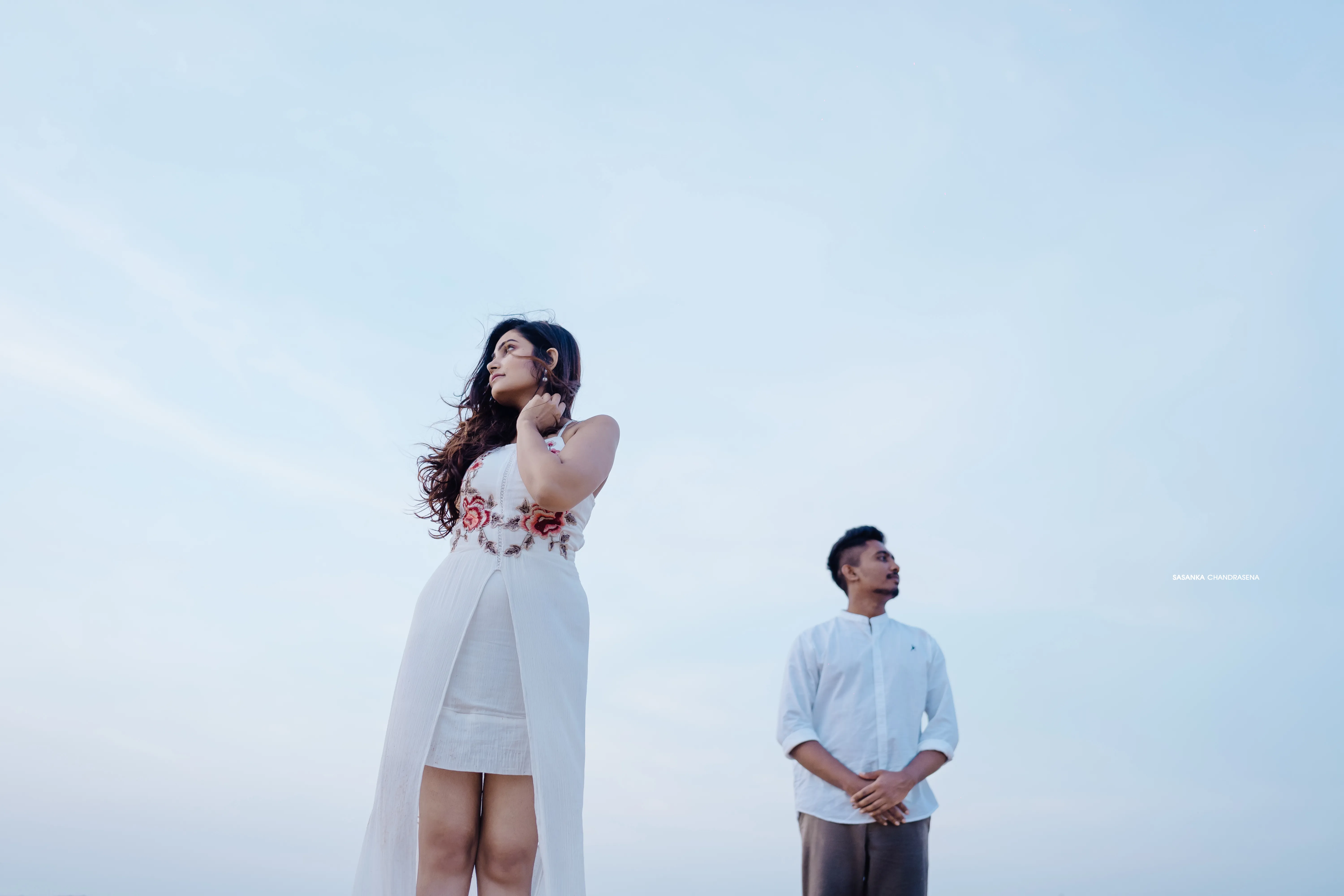 The couple stands apart on the wide shoreline in matching white.