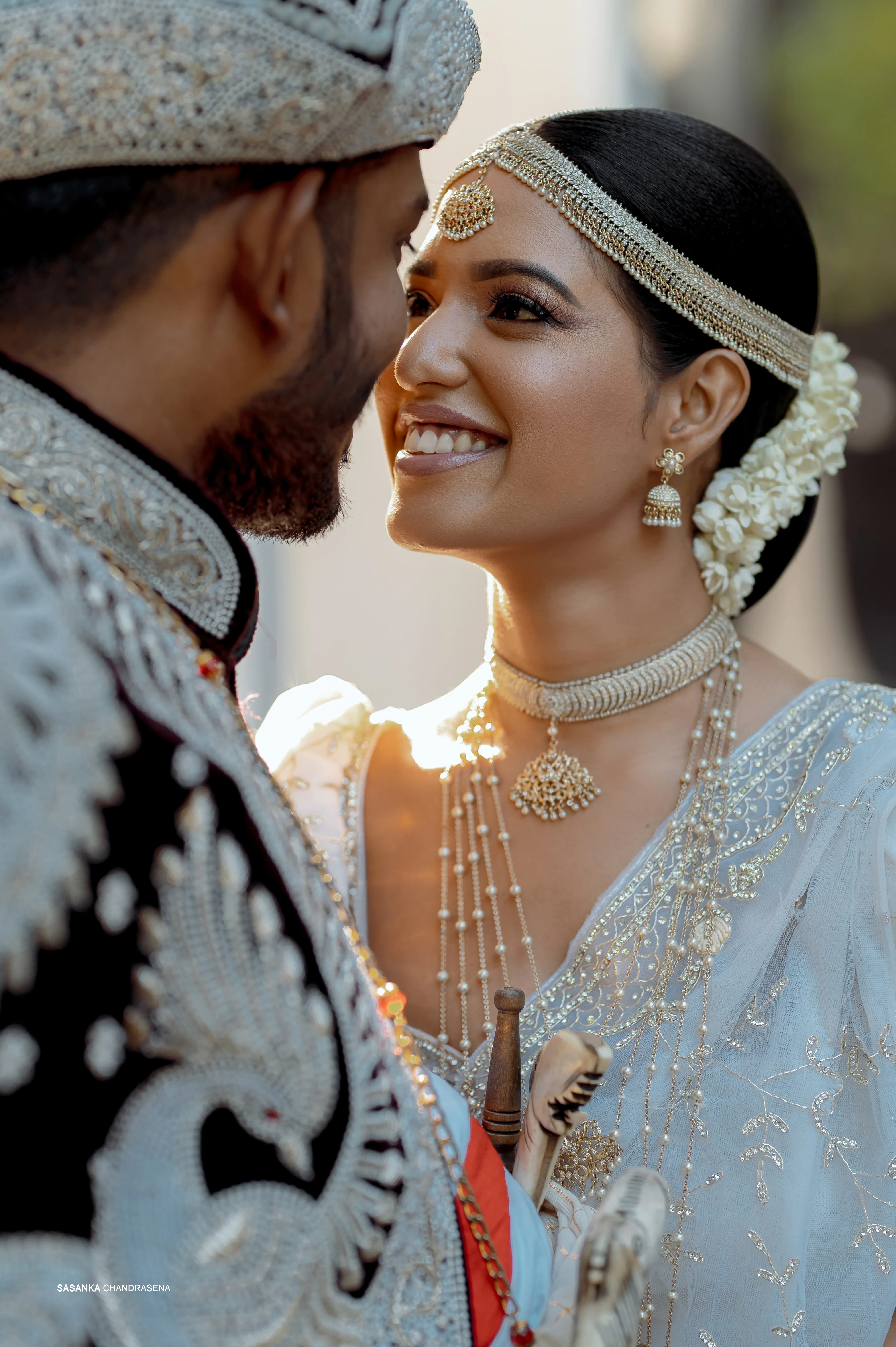 Warm sunlight catches Sachini’s jewelry as Shenuka leans close.