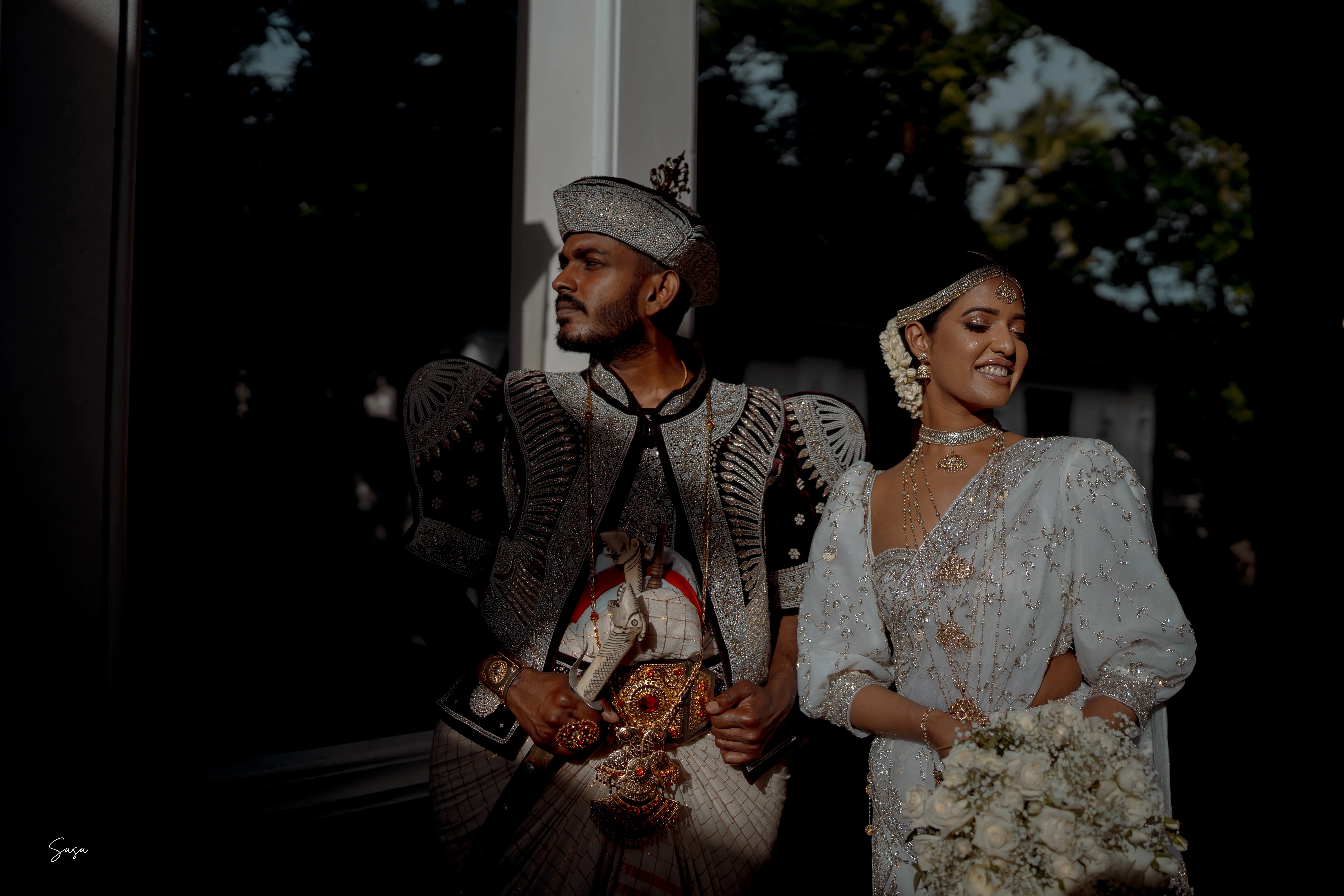 The couple shares an easy smile beneath the evening trees.