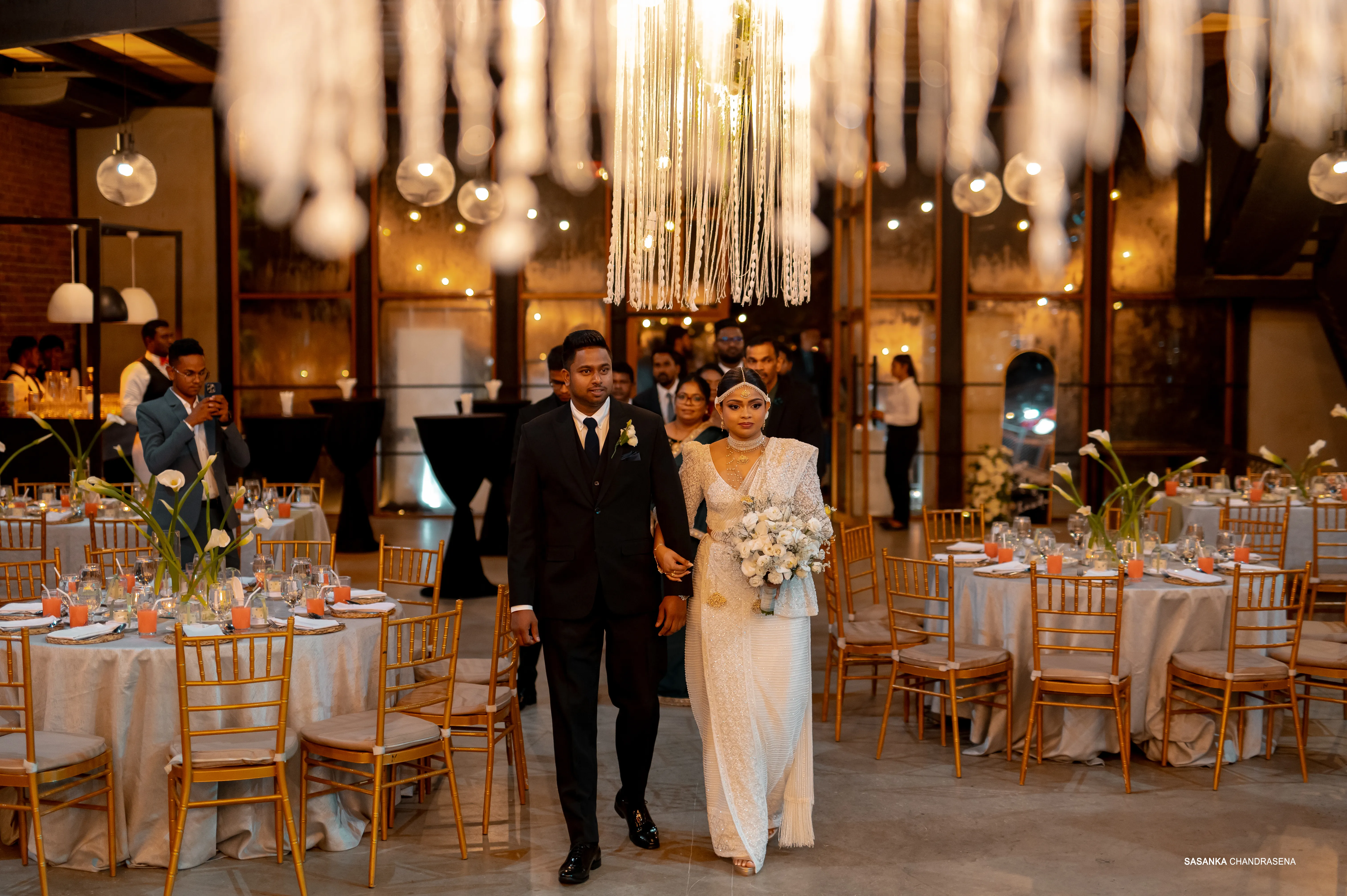The newlyweds enter the chandelier-lit reception accompanied by family.