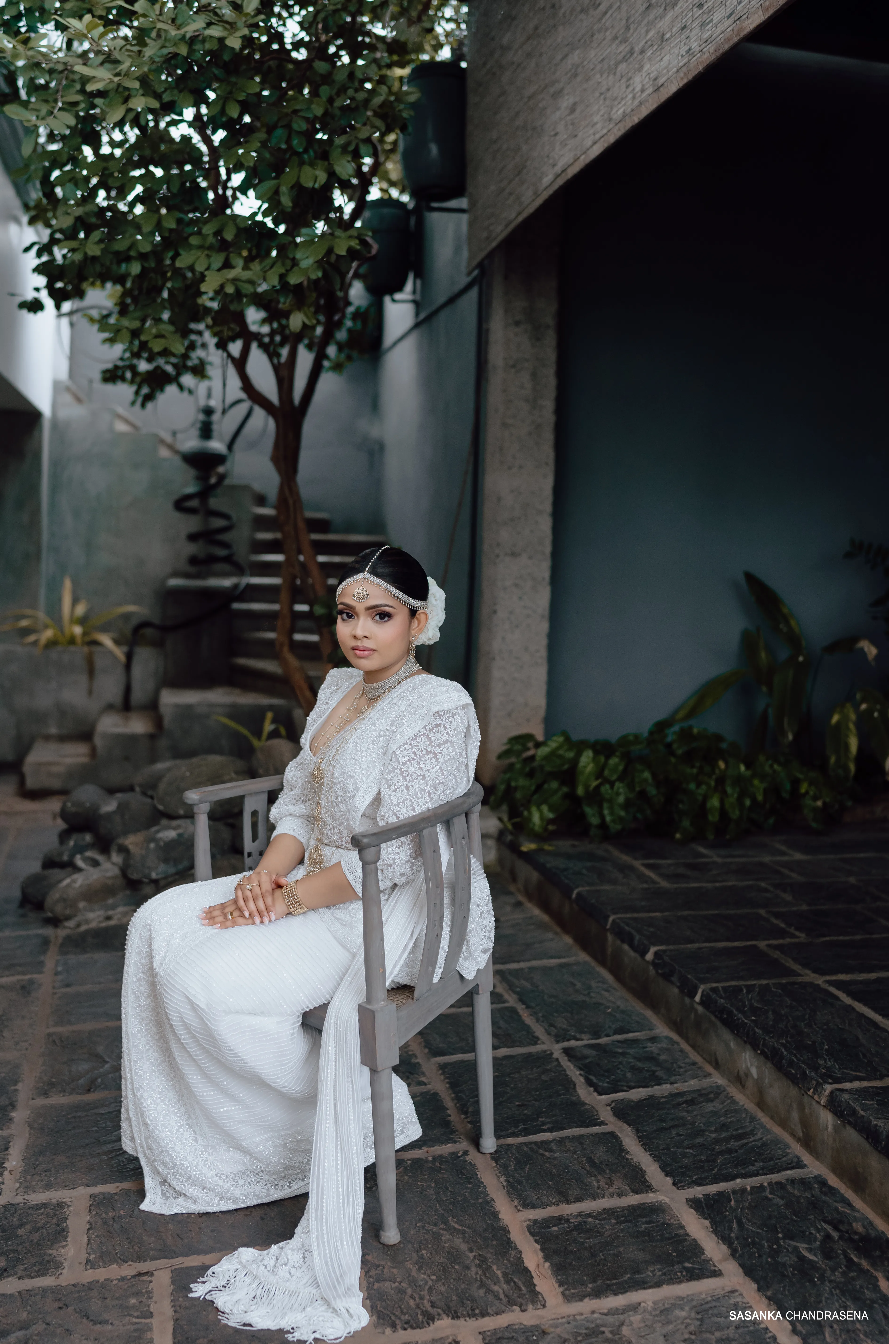 Tharu sits beside dark stone steps in an elegant full-length portrait.
