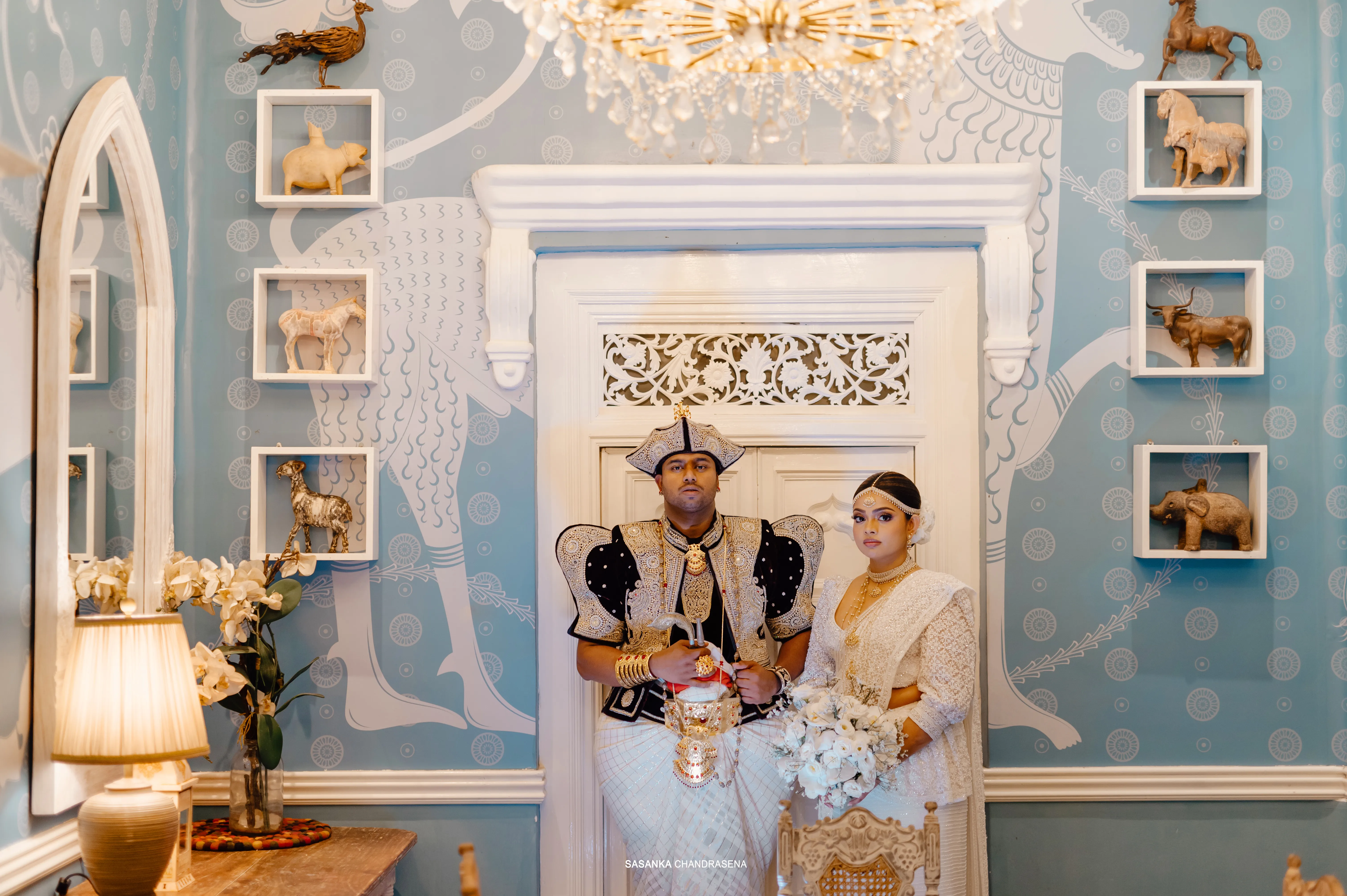 The newlyweds sit together in an ornate white reception room.