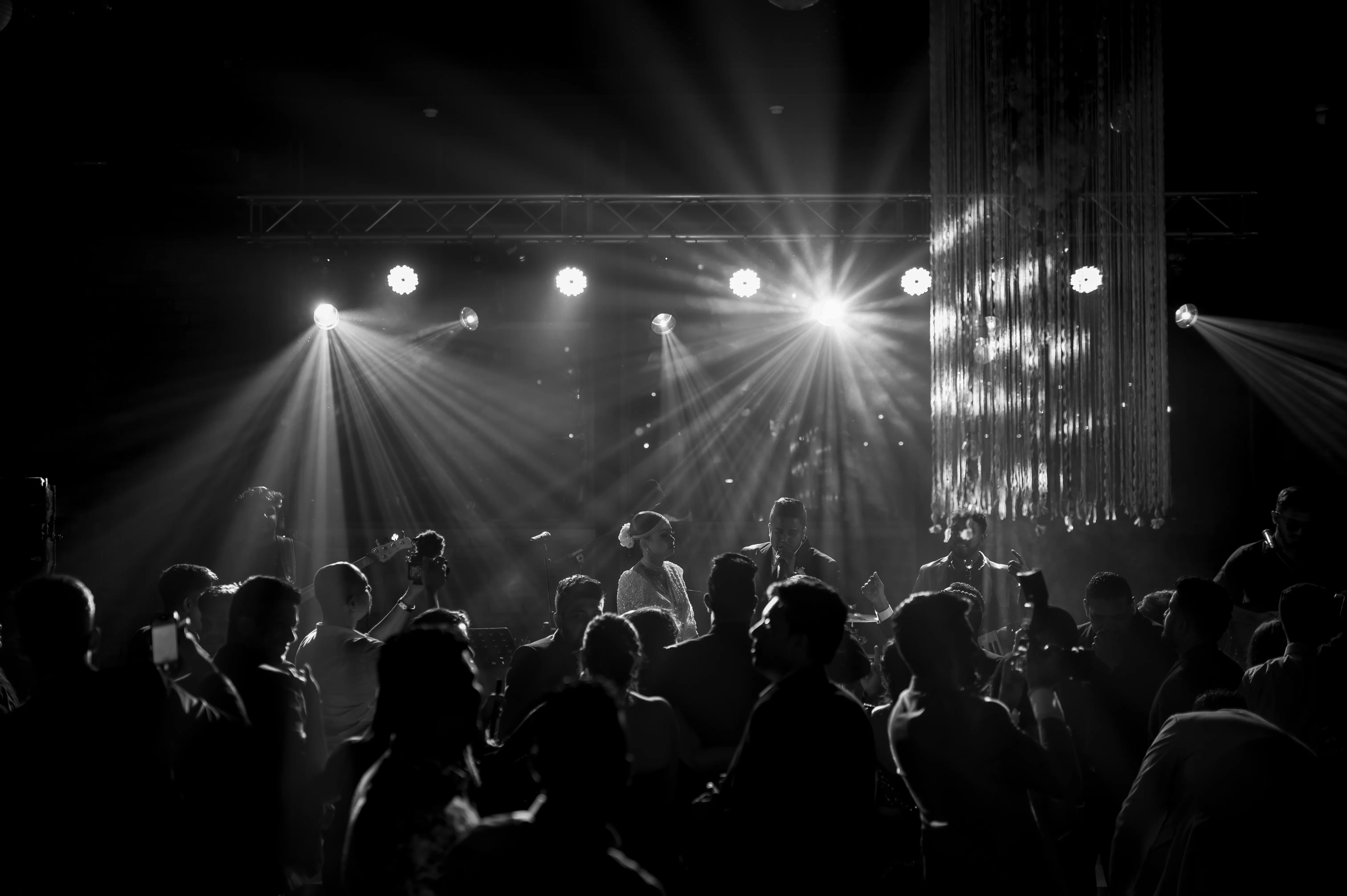 A monochrome crowd gathers beneath bright concert lights on the dance floor.