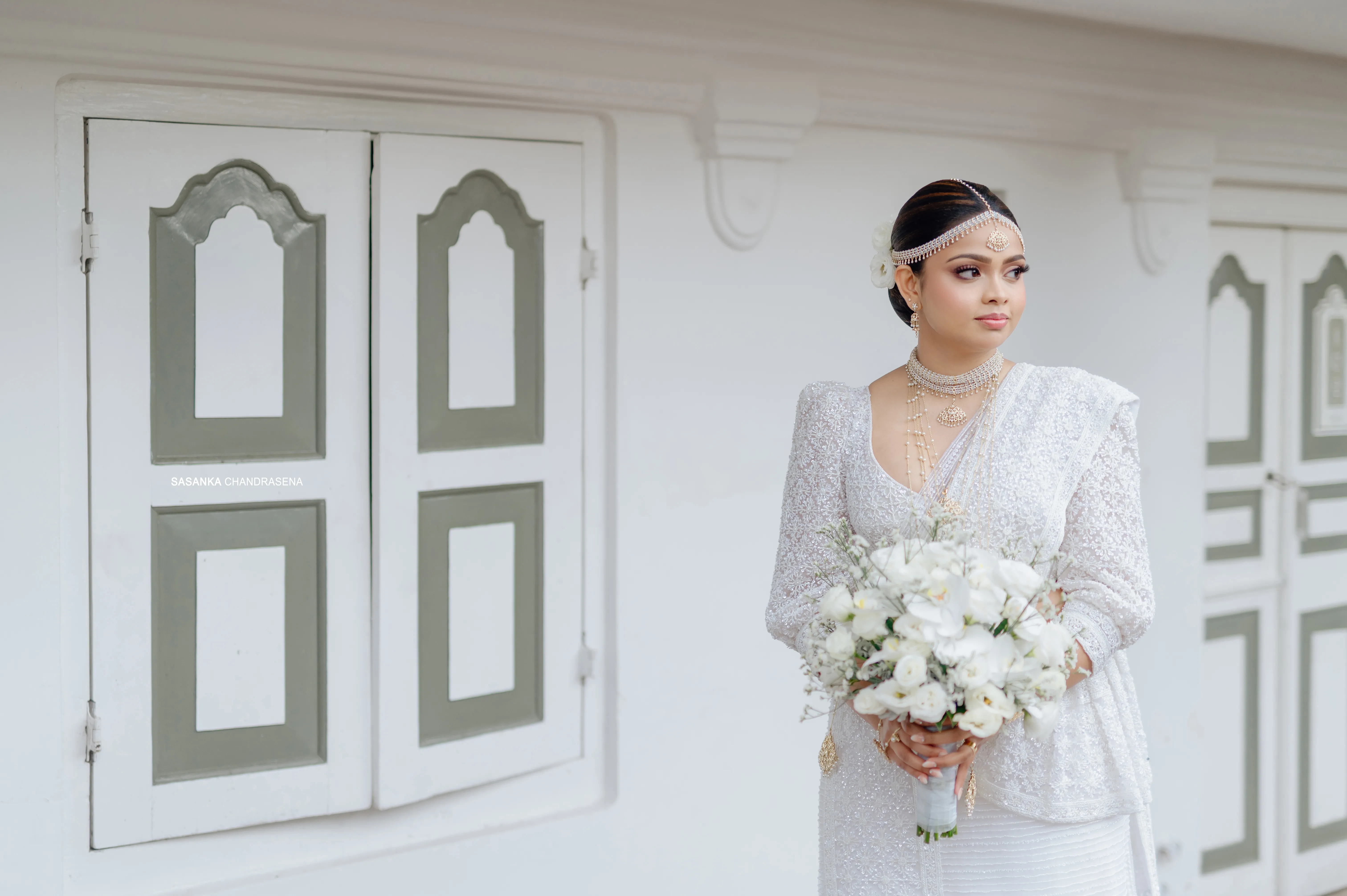 Tharu stands with her bouquet against sculpted white architecture.