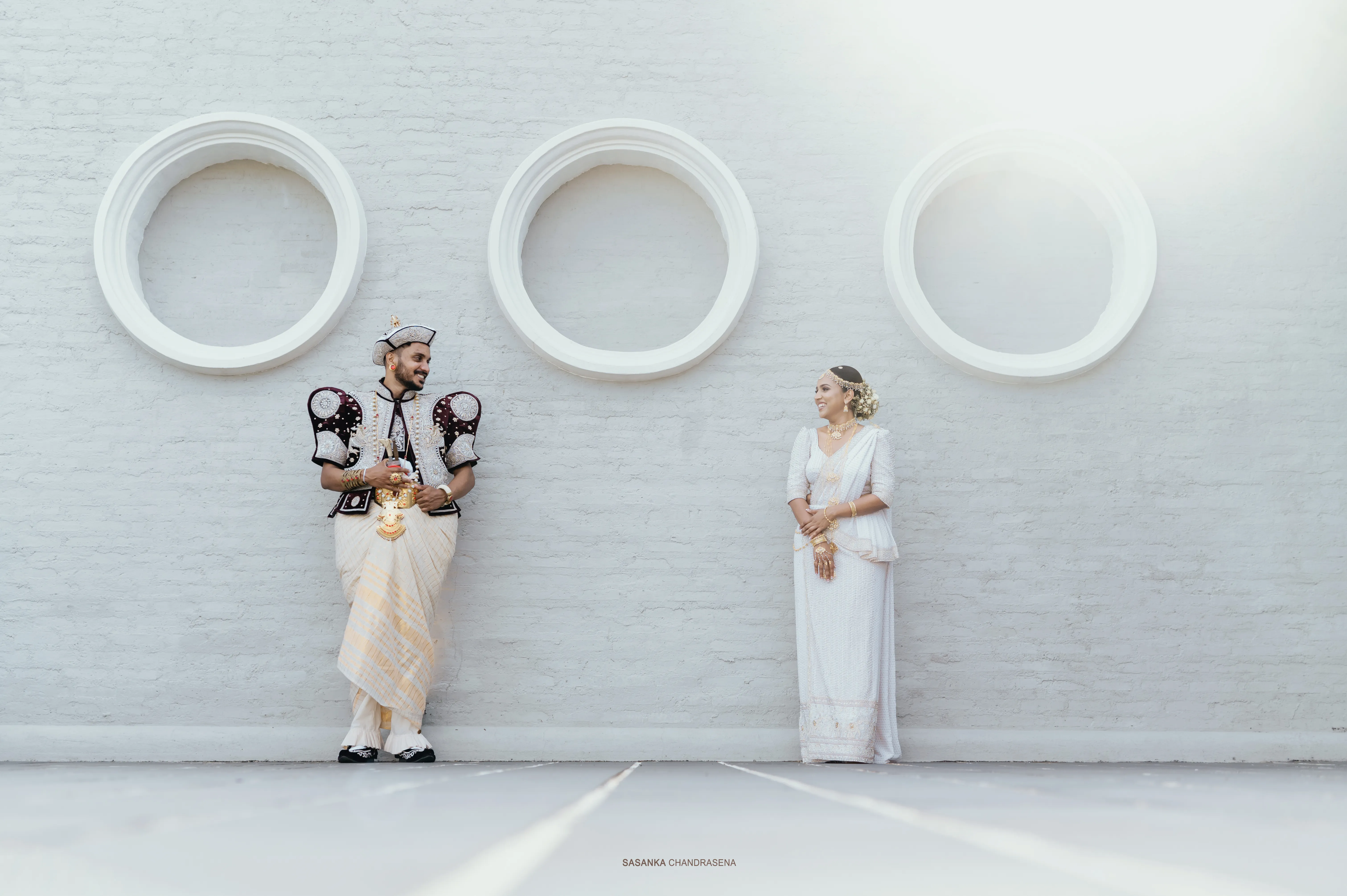 Yasiru and Malki stand apart beneath three sculptural round windows.
