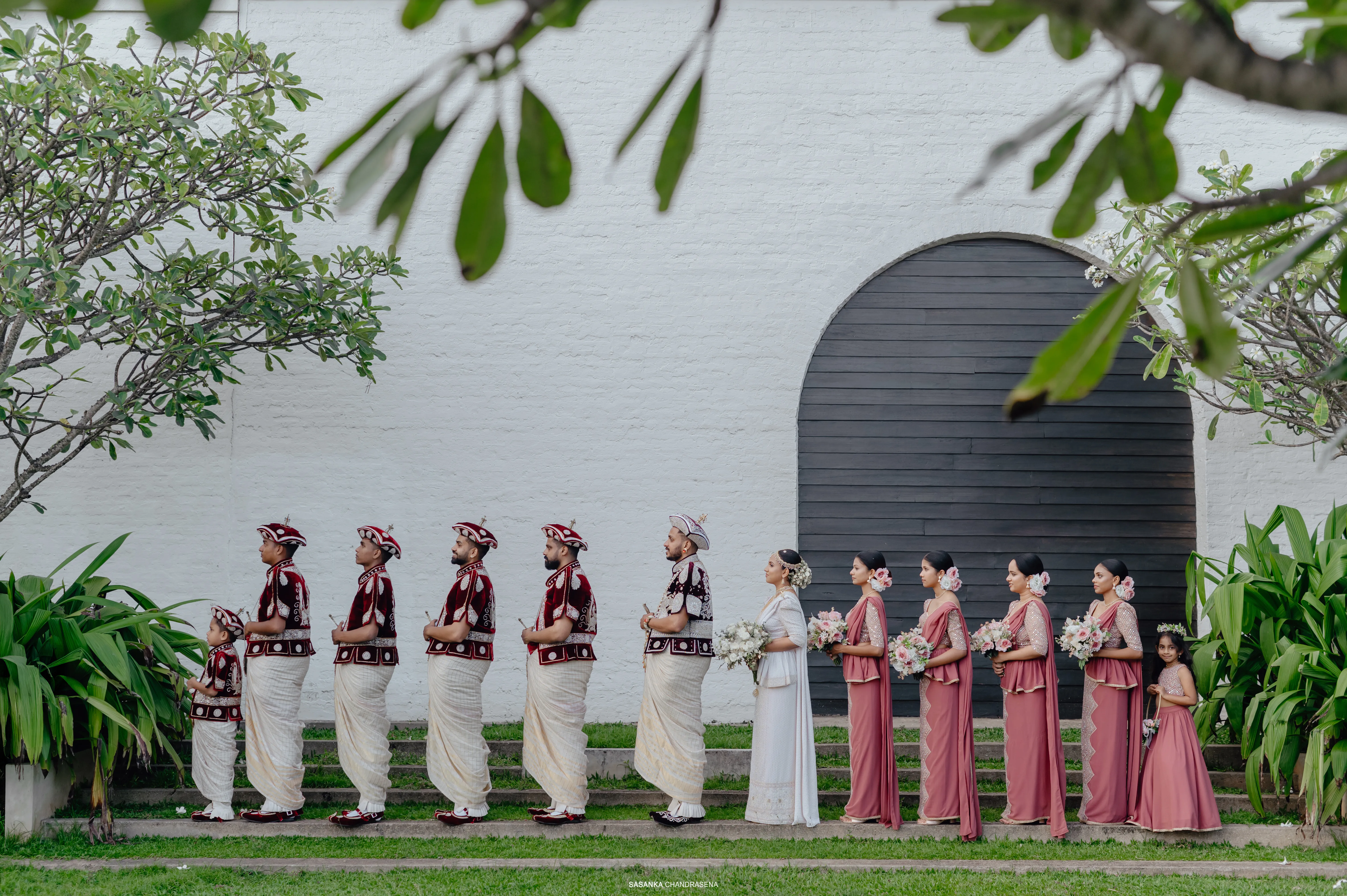 Members of the wedding party form a graceful line against the white wall.