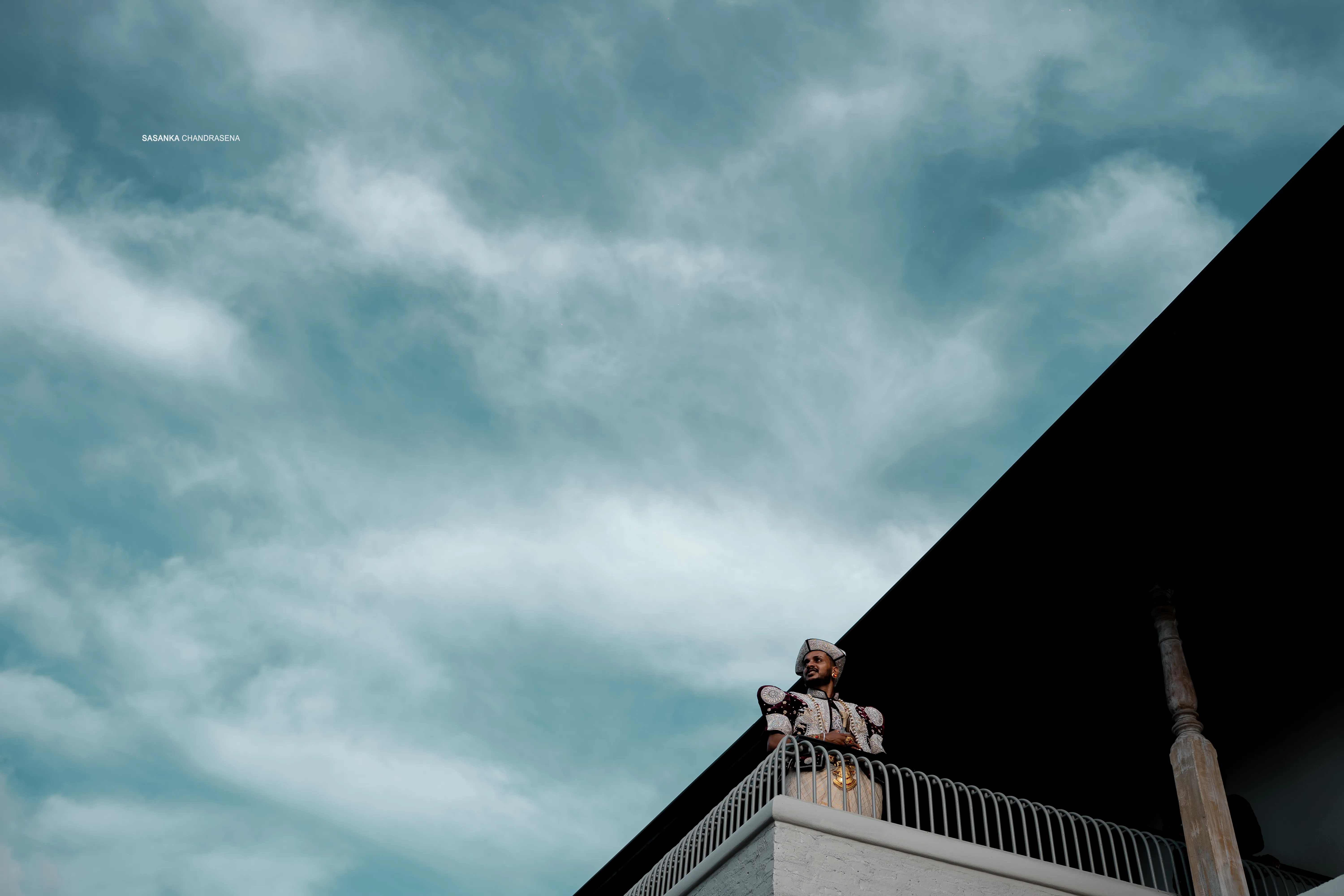 The newlyweds appear on a high terrace beneath a dramatic blue-grey sky.