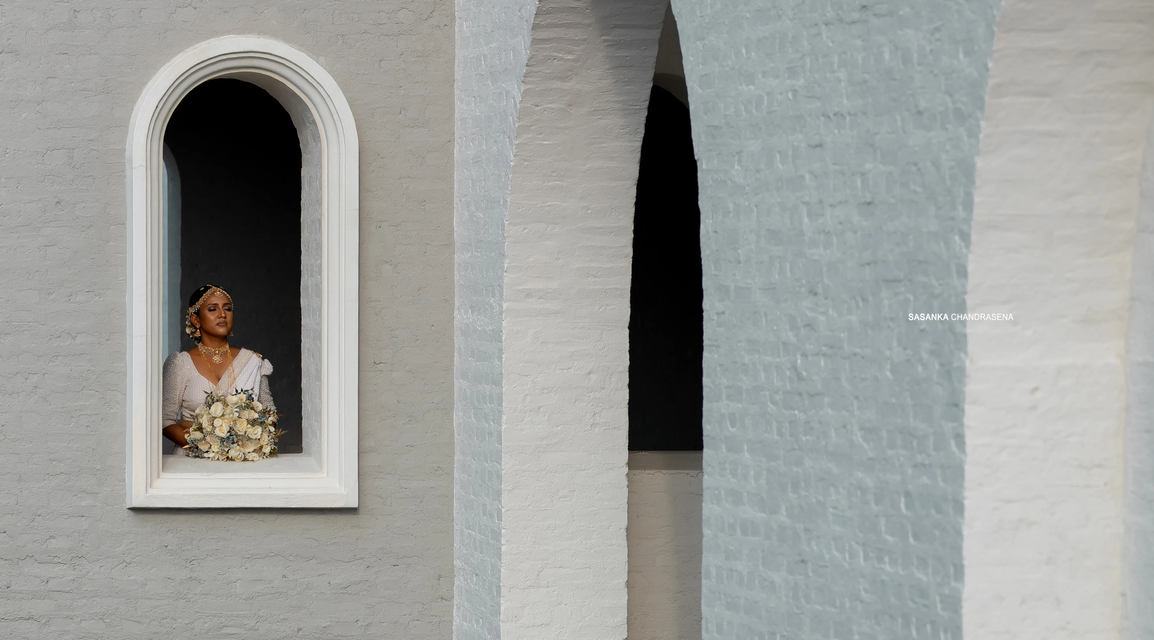 Malki holds her bouquet inside a narrow white arched window.