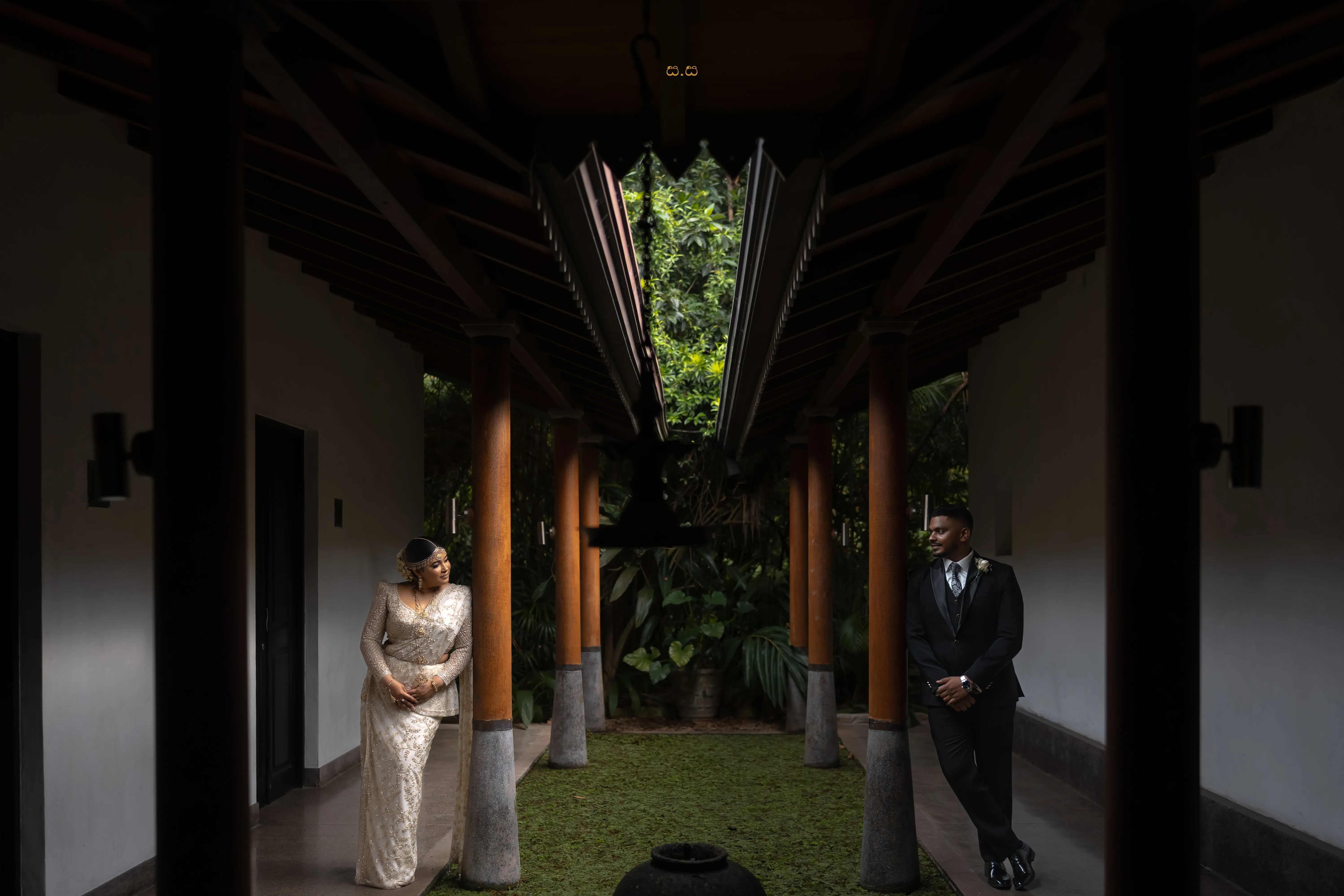 A Sri Lankan bride and groom facing each other across a shaded courtyard